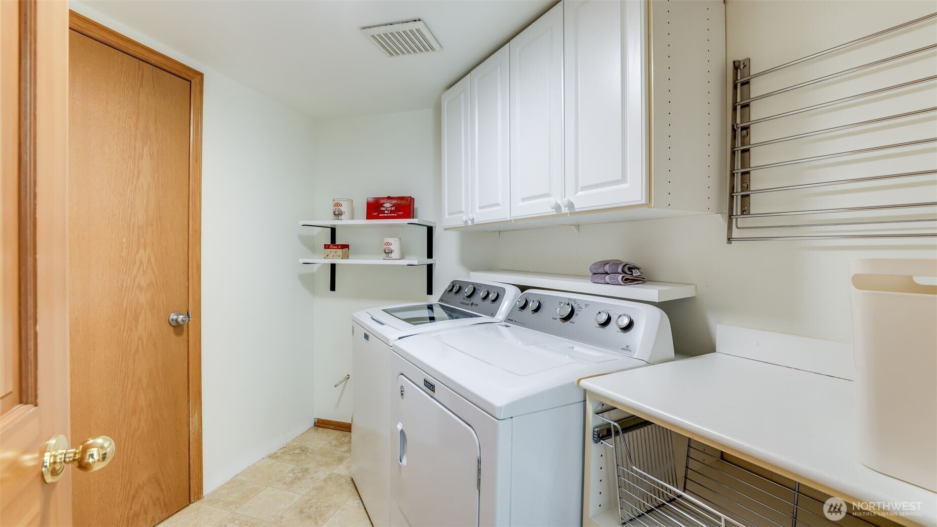 This highly functional laundry room offers abundant storage with built-in shelving, upper cabinets, and a convenient side rack for drying clothes. Washer and dryer are included, making this space both practical and move-in ready