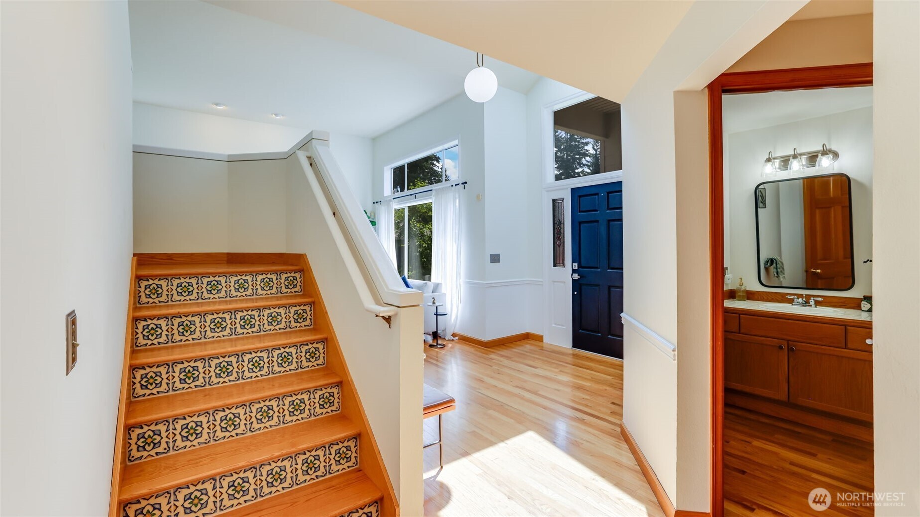This elegant staircase features stylish hardwood steps with decorative inlays for added flair. Conveniently located near the entrance, it leads to the upper level while offering a guest-friendly bathroom nearby for everyday ease