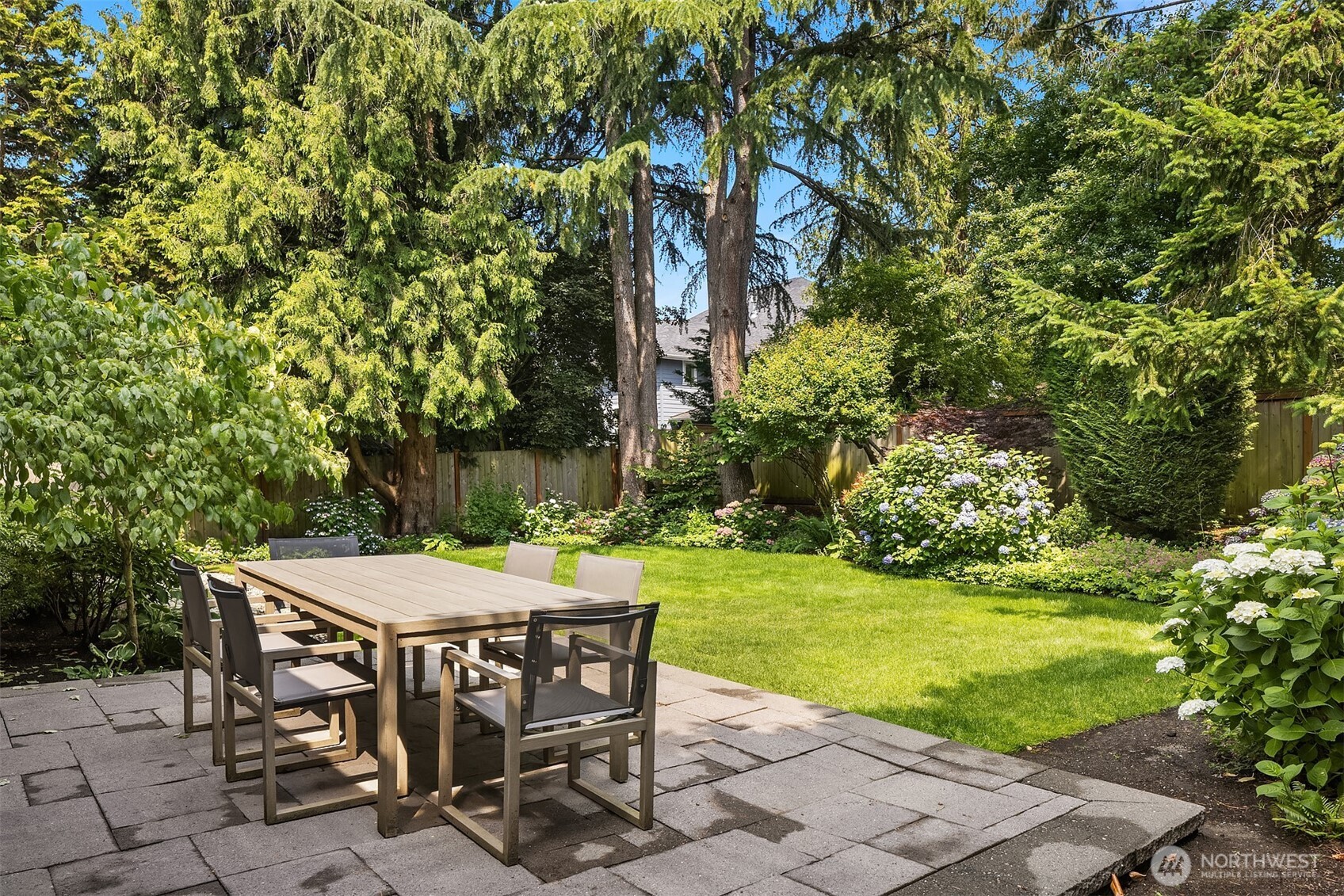 Lush, level, and beautifully private—this backyard is a true retreat. Host summer dinners on the paver patio surrounded by hydrangeas, mature evergreens, and vibrant landscaping that feels like your own secret garden.