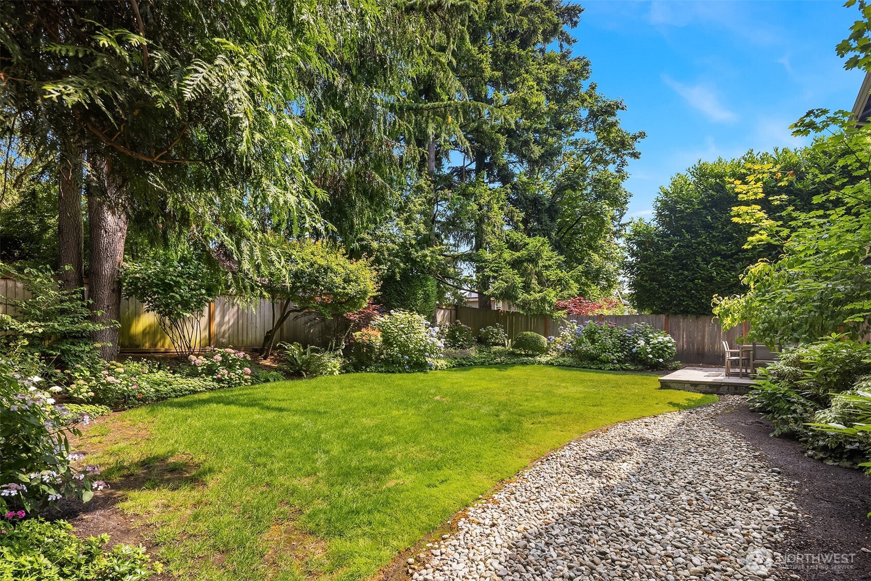 Framed by towering evergreens and vibrant hydrangeas, this fully fenced backyard is a true urban oasis—ideal for gardening, play, and peaceful morning coffee on the patio.