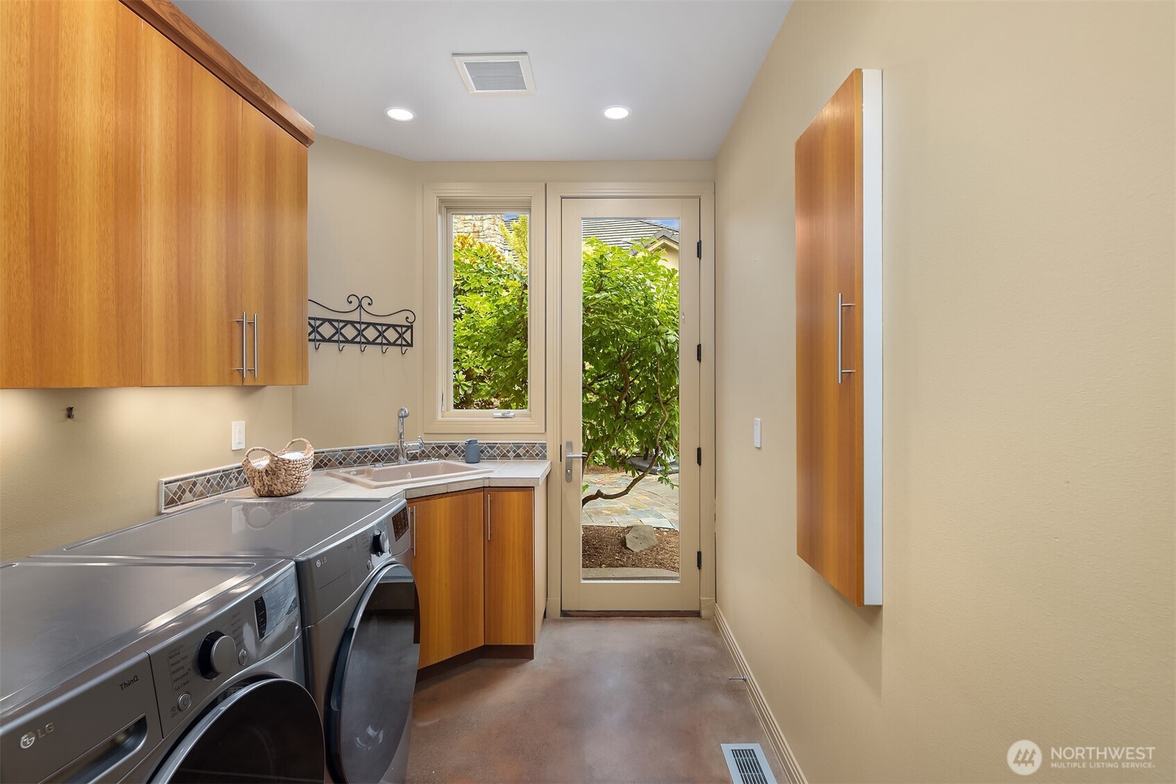 Spacious main floor laundry room with utility sink, wall ironing board, storage and door to driveway