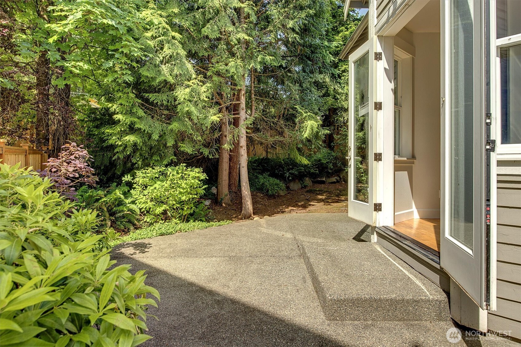 French doors off the breakfast nook open wide to a private, tree-lined patio, creating a seamless indoor-outdoor connection. This inviting space is framed by mature landscaping and dappled sunlight, offering both tranquility and privacy just steps from the kitchen.