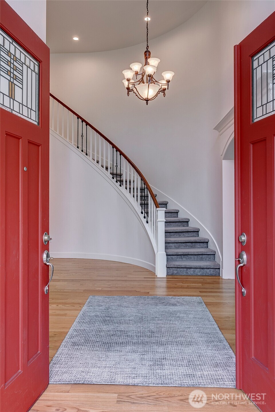 Step into a grand entryway with a dramatic curved staircase, elegant chandelier, and warm hardwood floors—setting the tone for the refined interiors beyond.