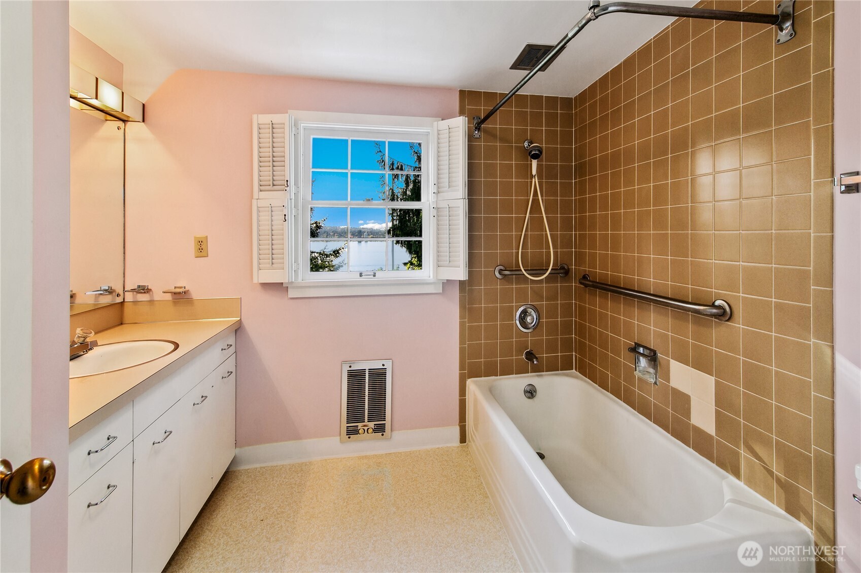 This vintage bath retains charming mid-century details, from the warm ceramic tile to the classic built-in vanity with double sinks. A shuttered window offers natural light and a peek at Lake Washington beyond, inviting calm reflection. With both a soaking tub and shower, the space is primed for restoration or ready to serve as a nostalgic nod to the home's enduring character.