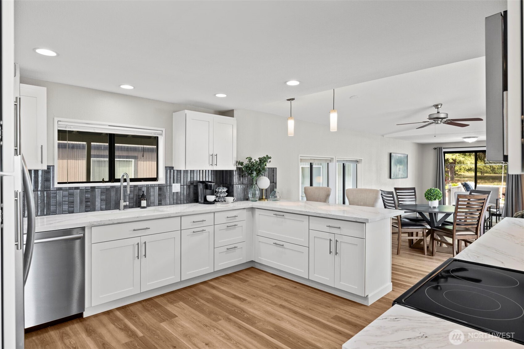 New kitchen with white soft closing cabinetry, quartz counter tops providing an abundance of food preparation space, stylish deco tile backsplash, stainless steel appliances, breakfast bar with pendant lighting, and eat in table space.