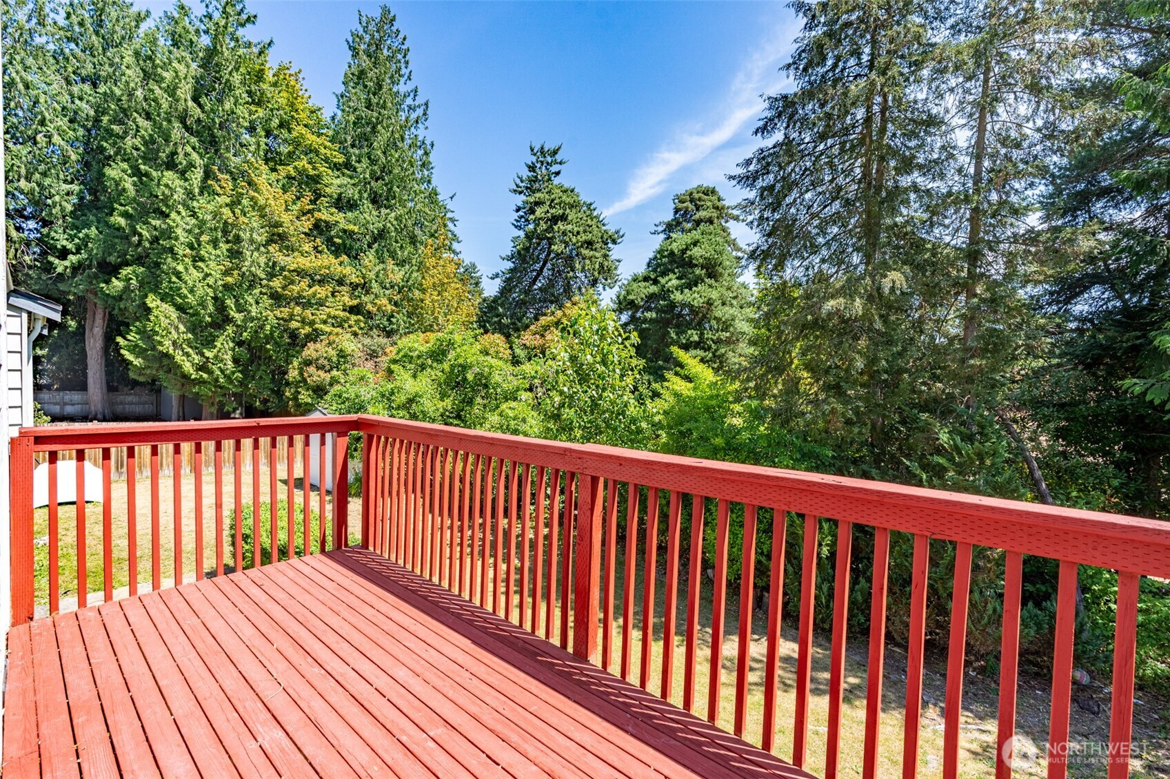 Delightful deck overlooks yard with a lush green backdrop.