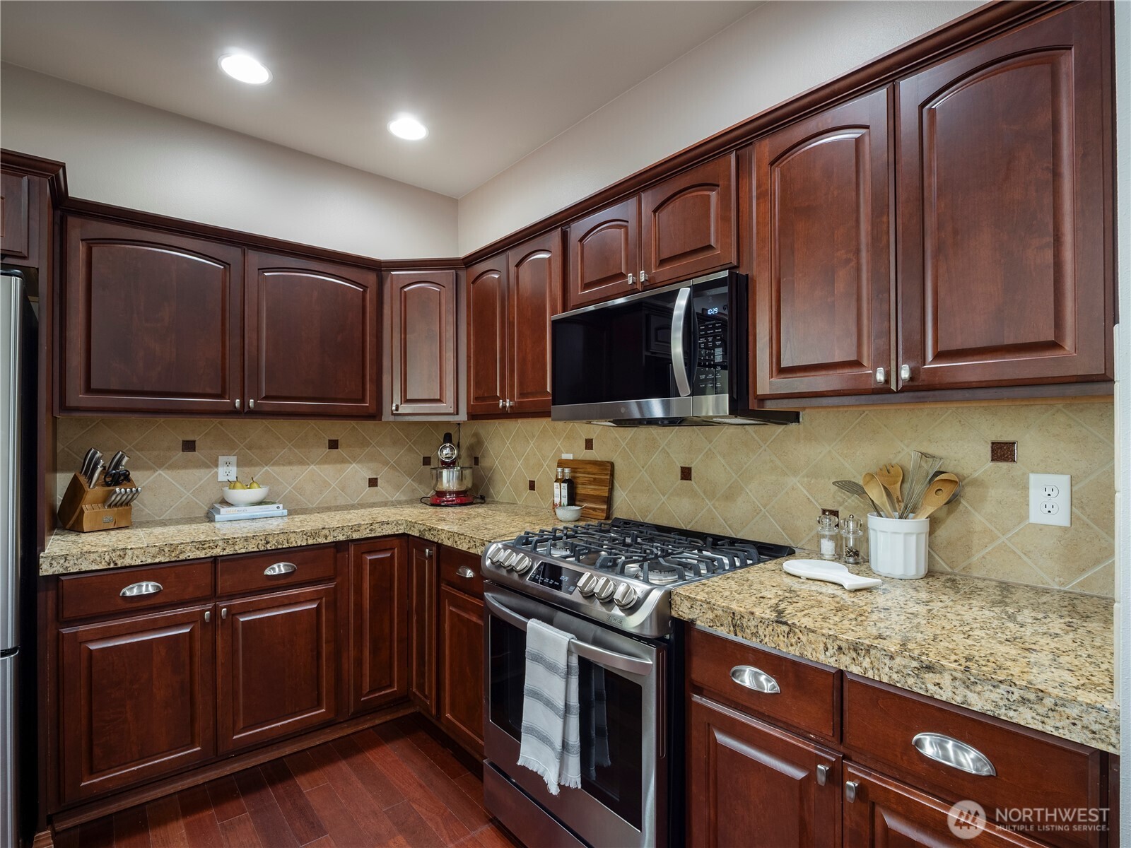 The kitchen features granite tile countertops, tile backsplash, gas range, stainless steel appliances and cabinets with pullout drawers.