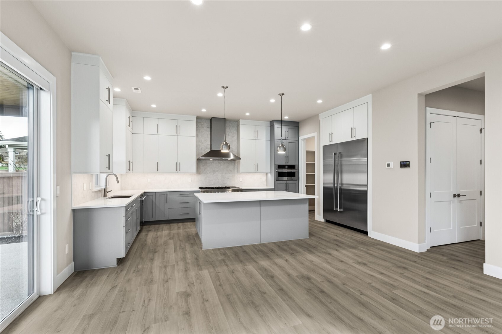Expansive modern kitchen with sleek quartz countertops, full-height cabinetry, oversized island, and walk-in pantry. Designer lighting and premium stainless steel appliances—including a built-in fridge and double ovens—complete this stunning culinary space.