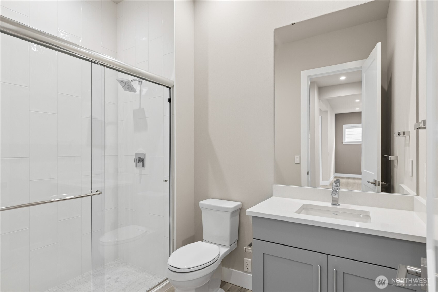 Full bathroom on the main level featuring a sleek tile-surround shower with glass enclosure, quartz countertop, and modern gray vanity—perfectly situated for guests.