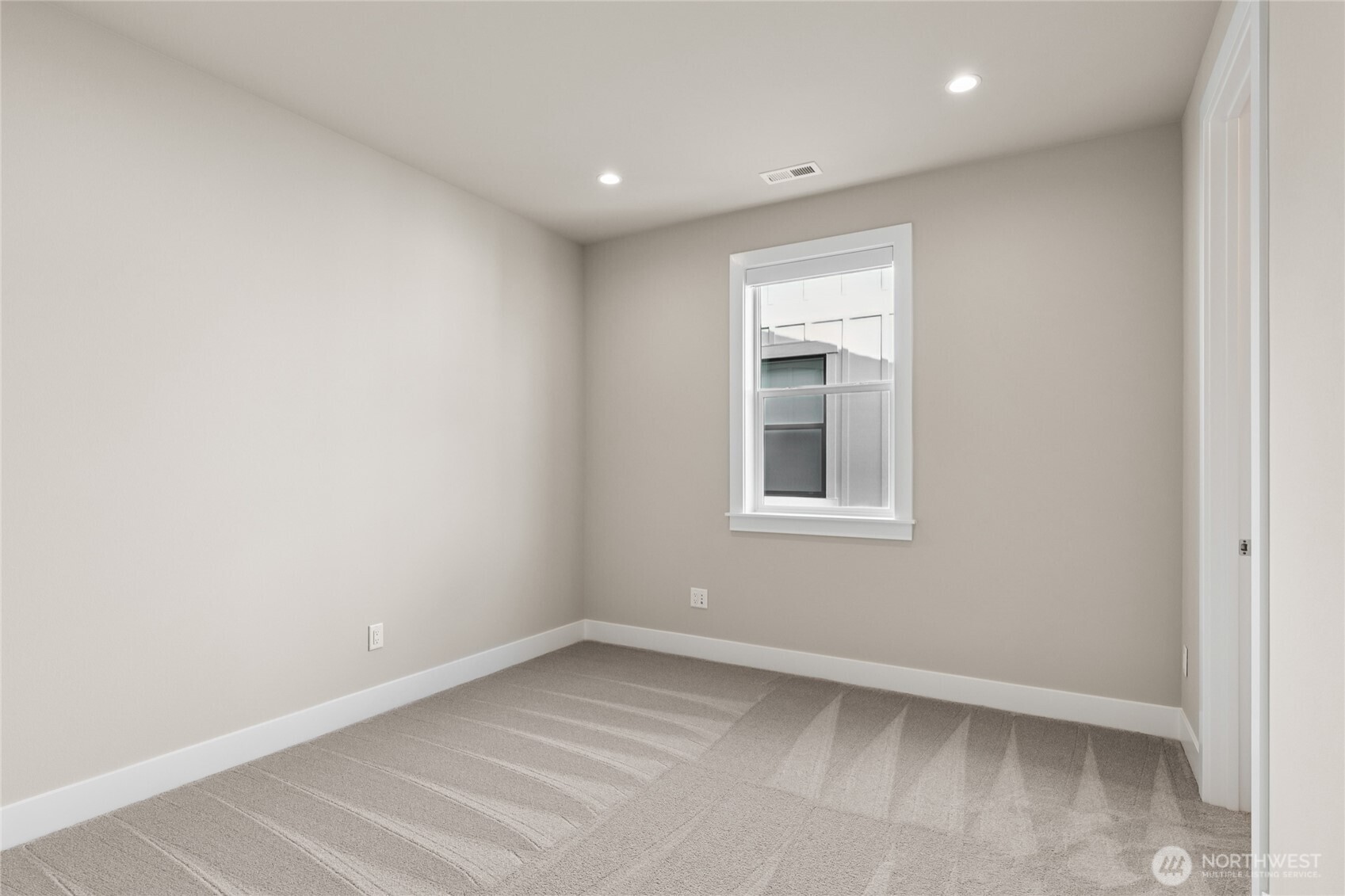 Cozy bedroom with soft neutral tones, plush carpeting, and recessed lighting. A large window provides natural light and a peaceful setting—perfect for a guest room, office, or additional sleeping space.