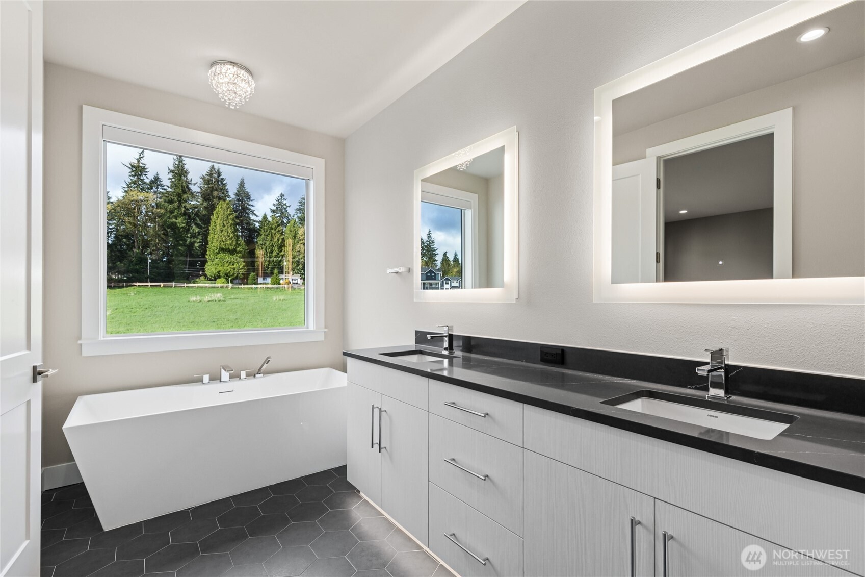 Luxurious primary bath featuring a modern dual-sink vanity with quartz counters, backlit mirrors, and a freestanding soaking tub positioned beside a large picture window—offering a serene and spa-like retreat.