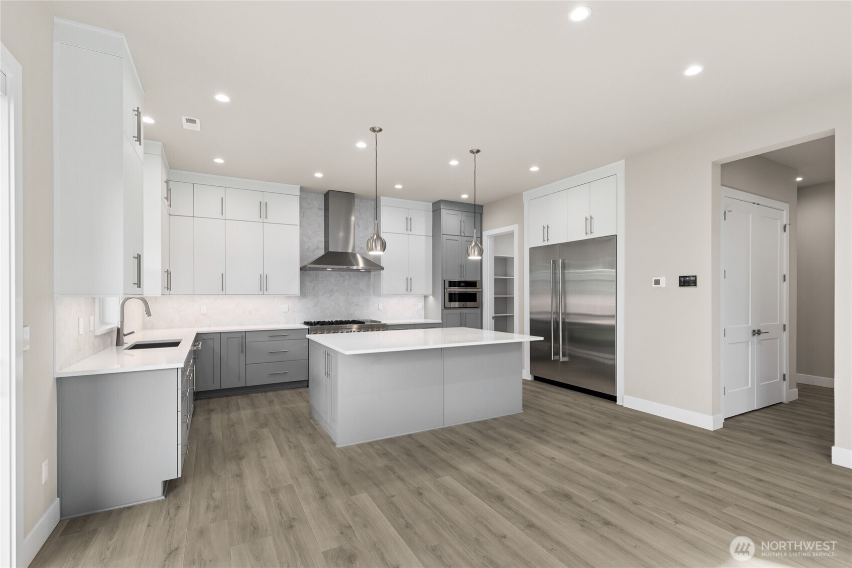 Chef-inspired kitchen with a large center island, custom two-tone cabinetry, commercial-style range hood, double ovens, and a built-in fridge. Bright, modern finishes and ample storage make this space both functional and stunning.