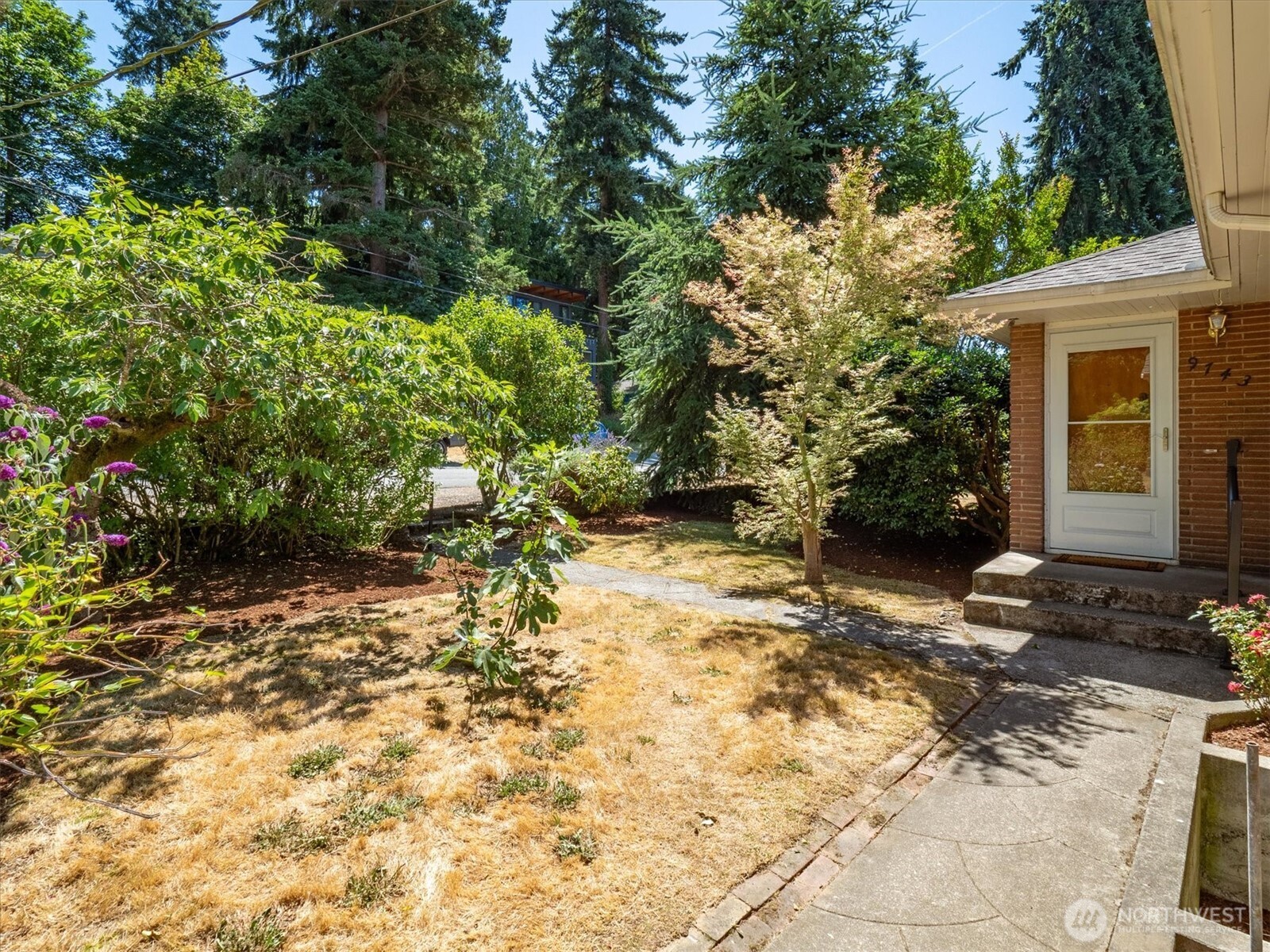 Semi-private and wholly beautiful, the front yard leads to the beautiful brick exterior of this Matthews Beach home.