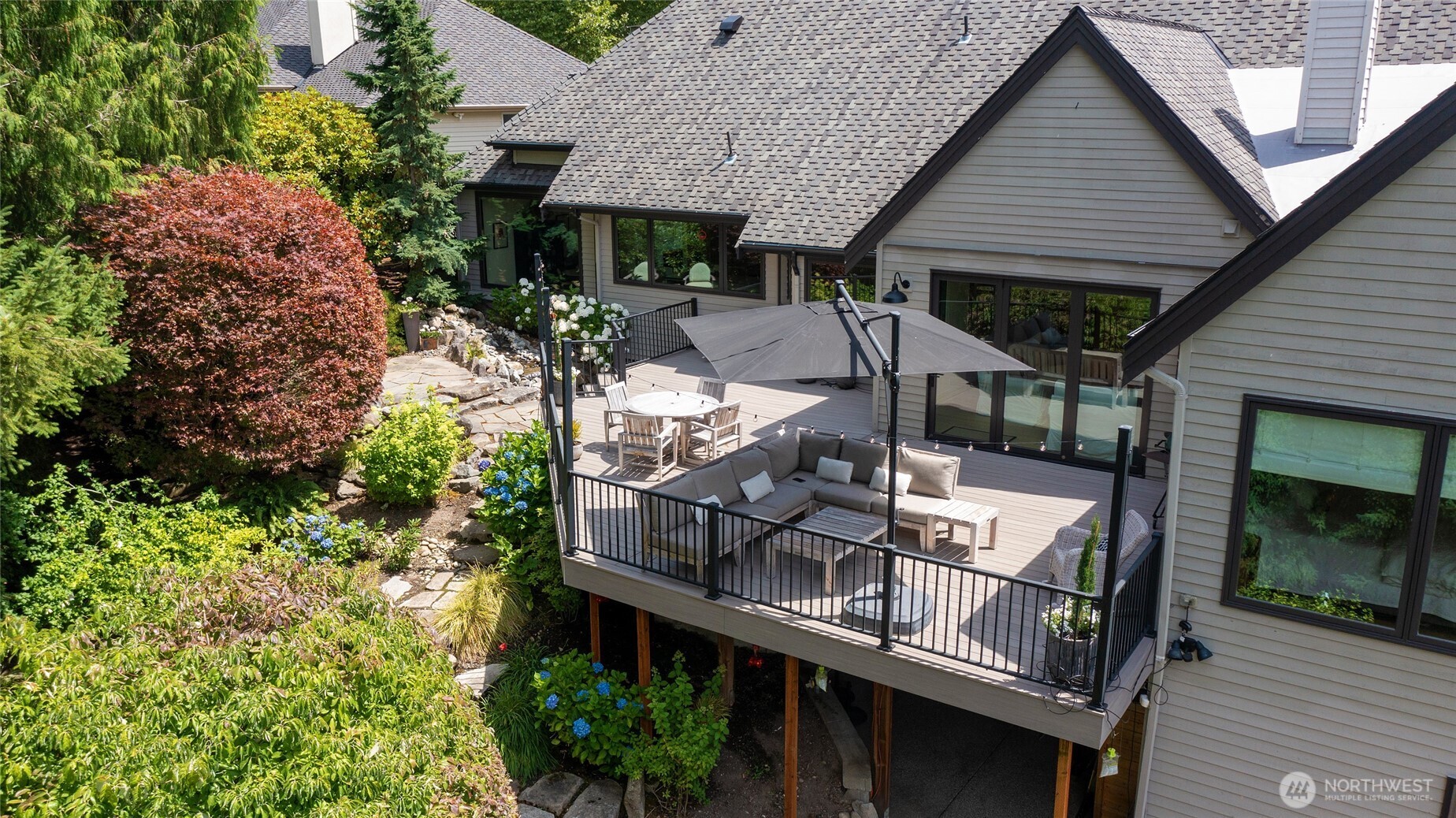 Stunning aerial view of the expansive entertaining deck and professionally landscaped backyard, complete with stone pathways, vibrant gardens, and a tranquil water feature—all offering exceptional outdoor living.