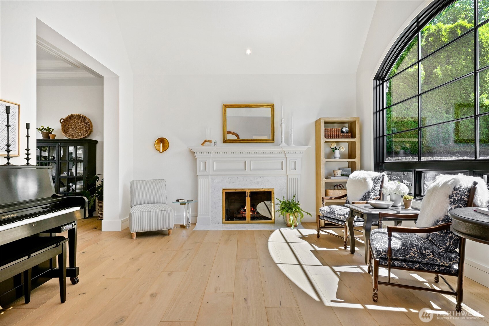 Sophisticated formal living room showcases a marble fireplace, vaulted ceilings, and stunning floor-to-ceiling arched window—perfectly blending classic elegance with modern light-filled design.
