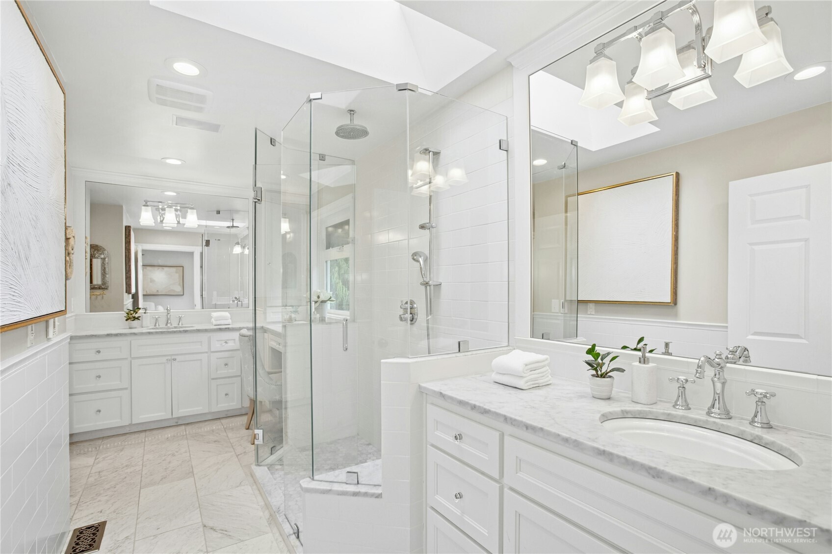 Spa-inspired retreat featuring heated floor, dual marble-topped vanities, frameless glass shower, and designer lighting beneath a skylit ceiling.