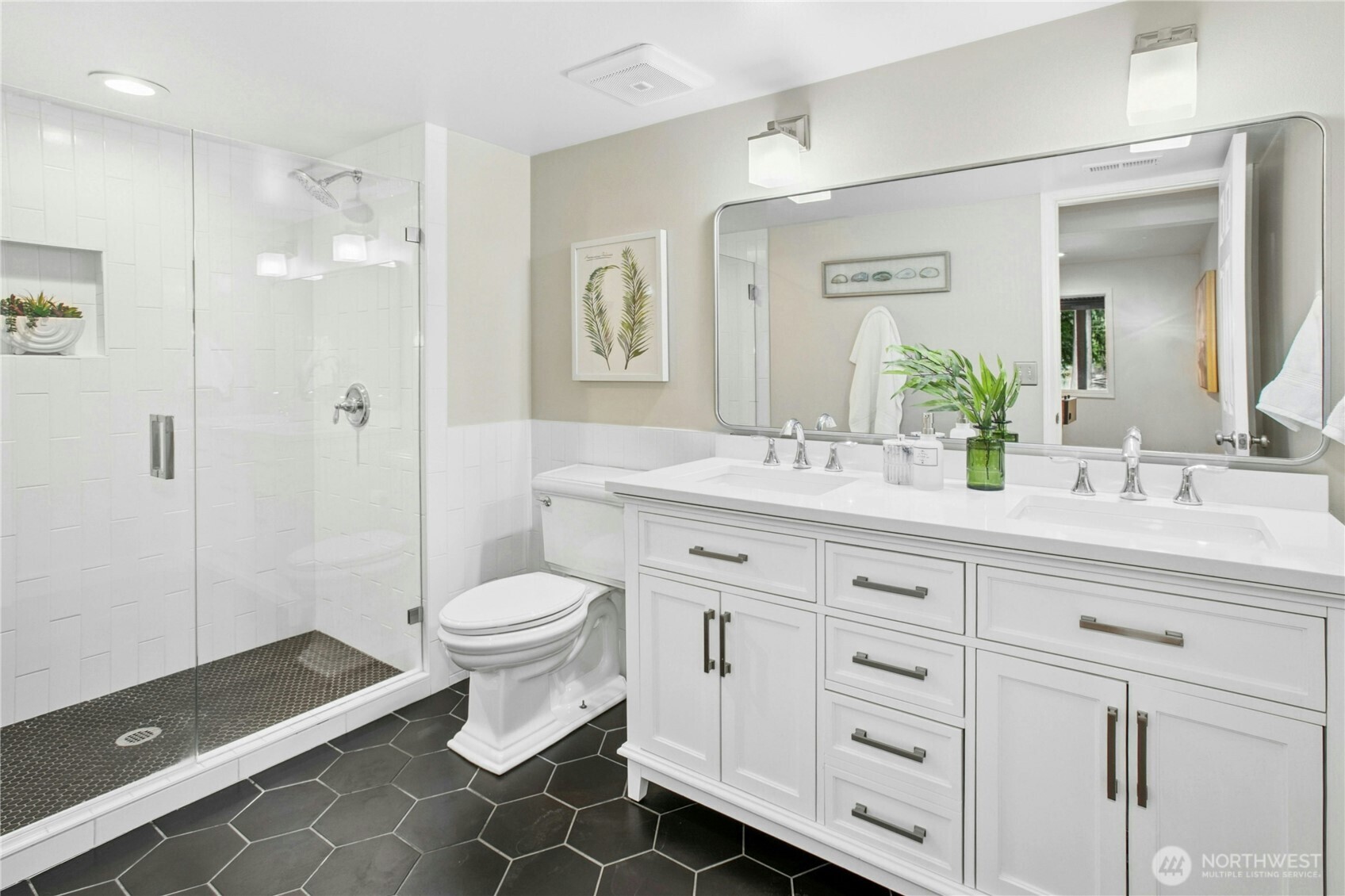 Stylishly updated 3/4 bathroom with dual vanity, designer tile, and frameless walk-in shower on the lower level, adjacent to the guest bedroom.