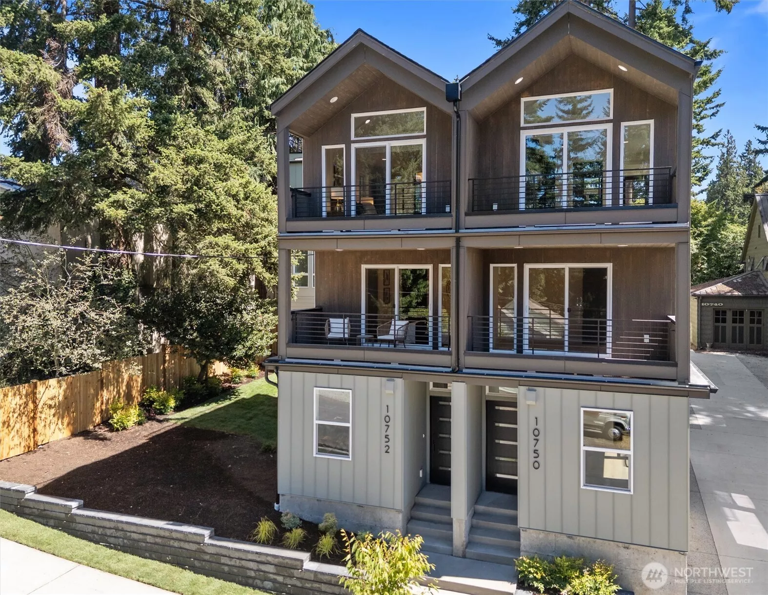 Contemporary dual-unit residence featuring expansive windows and private balconies set against a lush treed backdrop.