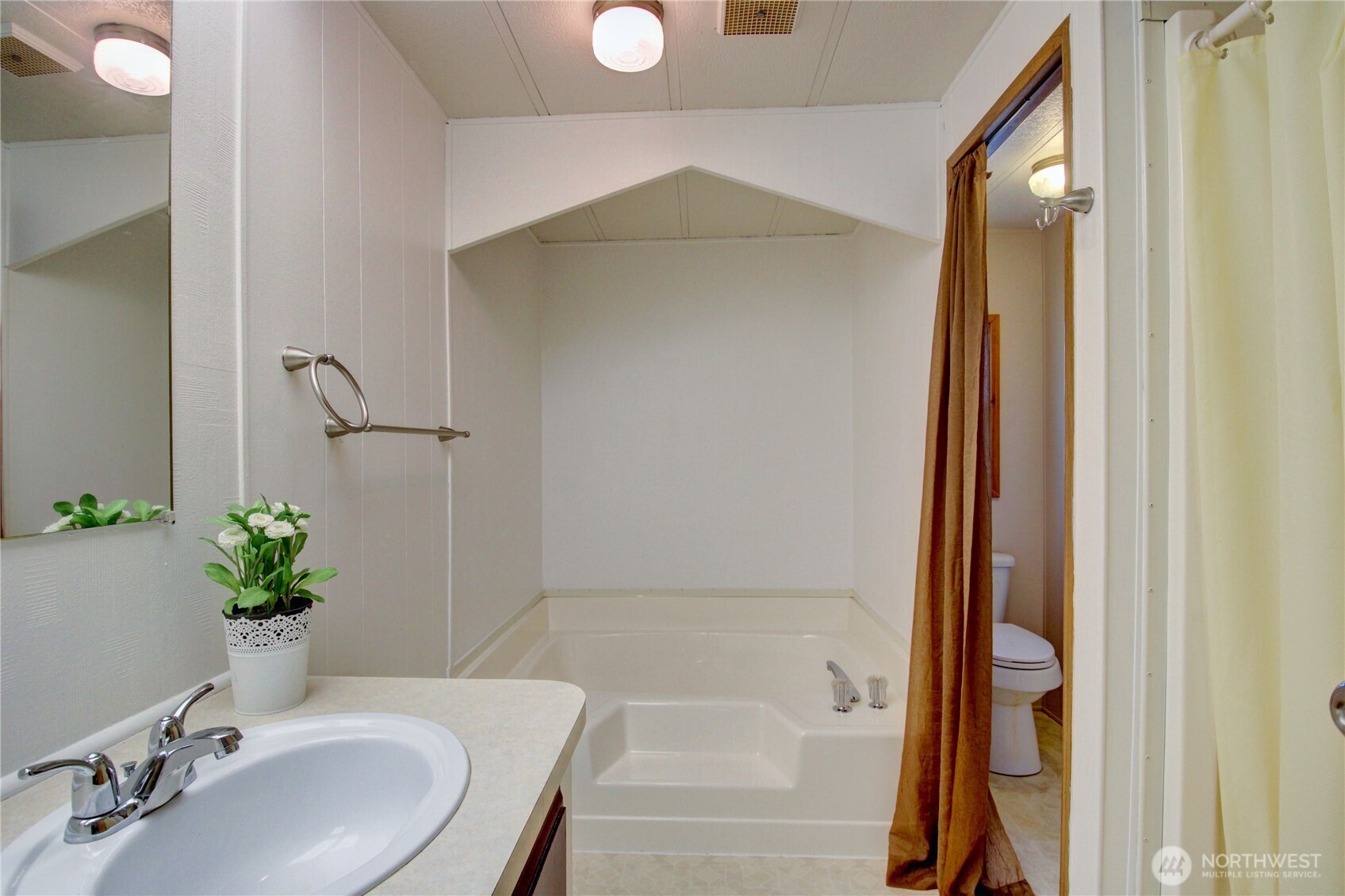 Primary bath has soaking tub and separate shower to the right.  Toilet is tucked away with curtain door.