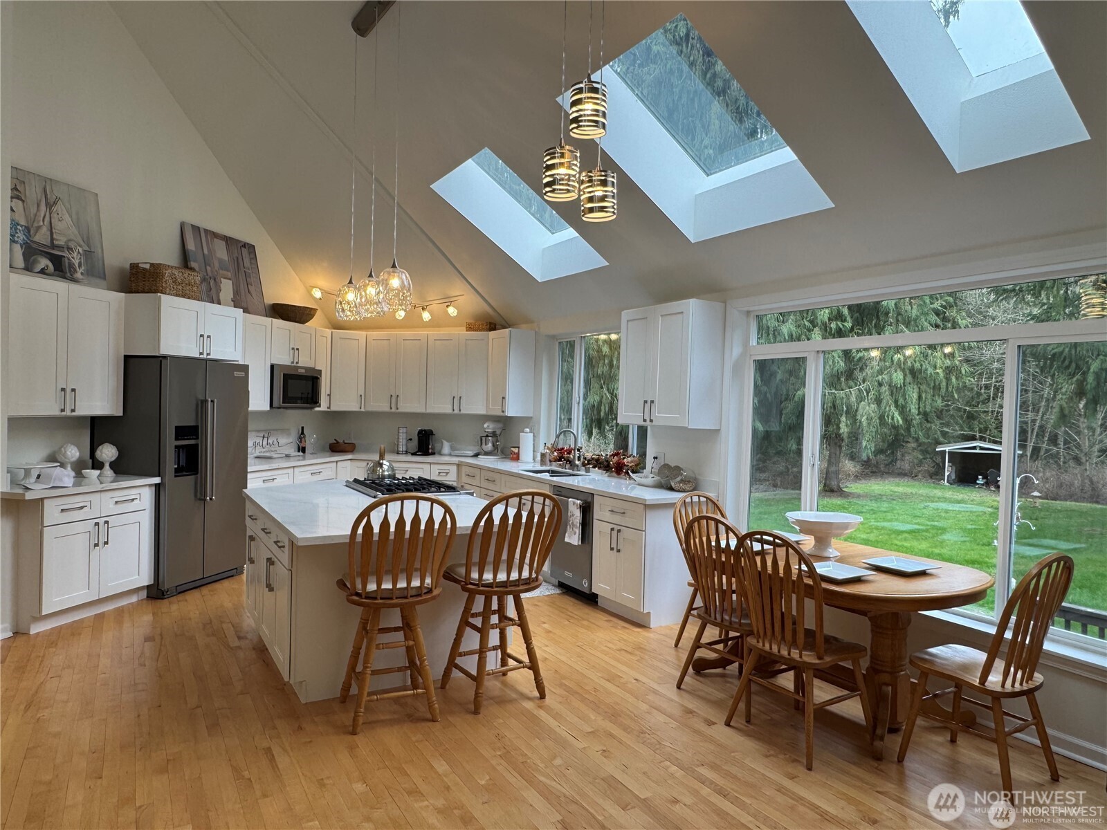 Beautiful open-concept gourmet kitchen featuring three new custom skylights and floor to ceiling windows that fill the space with natural light, while offering stunning views of the park-like grounds, rich hardwood floors, custom cabinets, new sleek quartz countertops, all new stainless steel appliances, custom lighting - perfect for everyday living and entertaining.