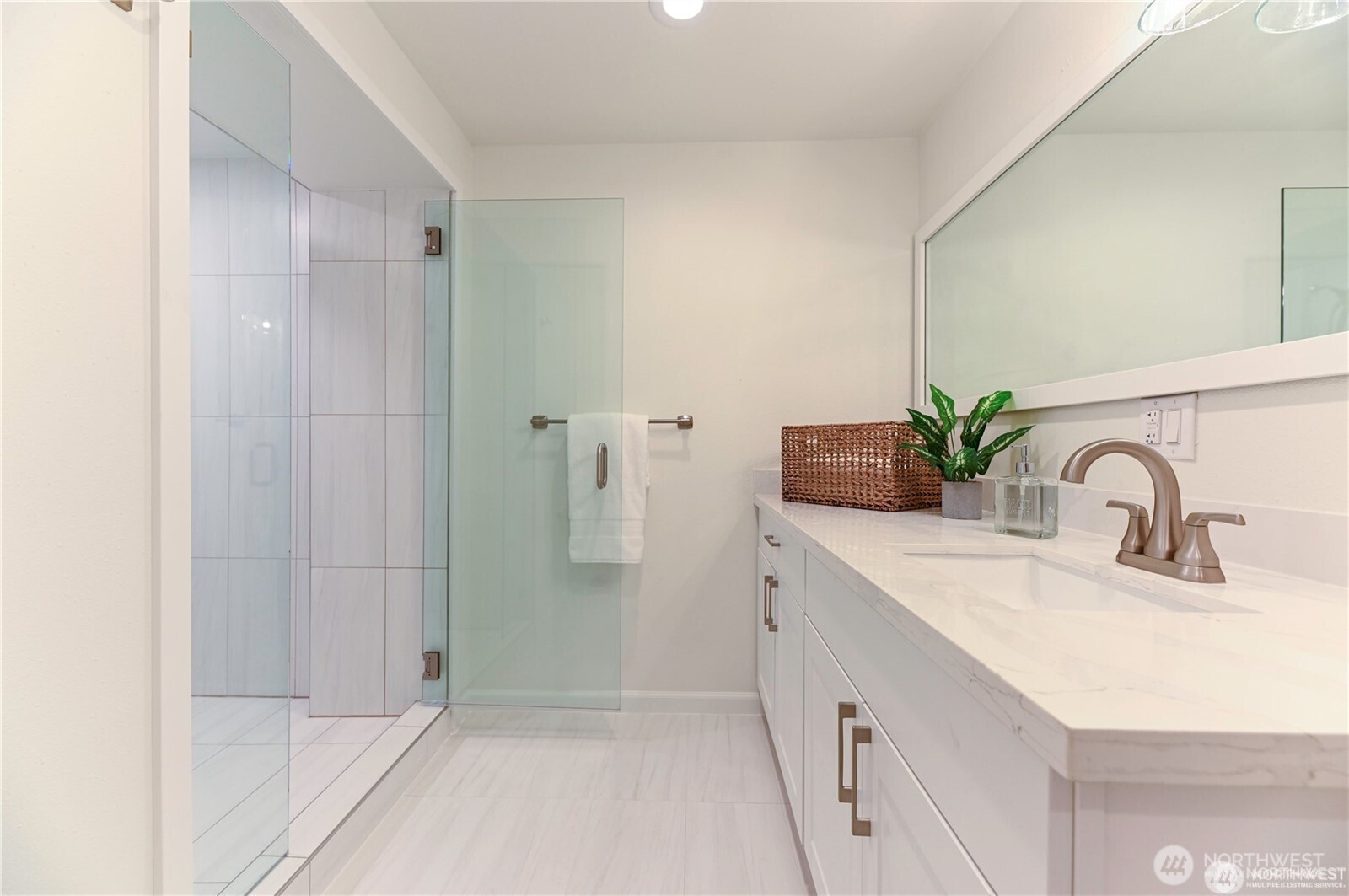 This full bathroom features a custom large oversized shower and glass door, new cabinetry, custom lighting, tiled floors and oversized sleek quartz countertops and mirror.