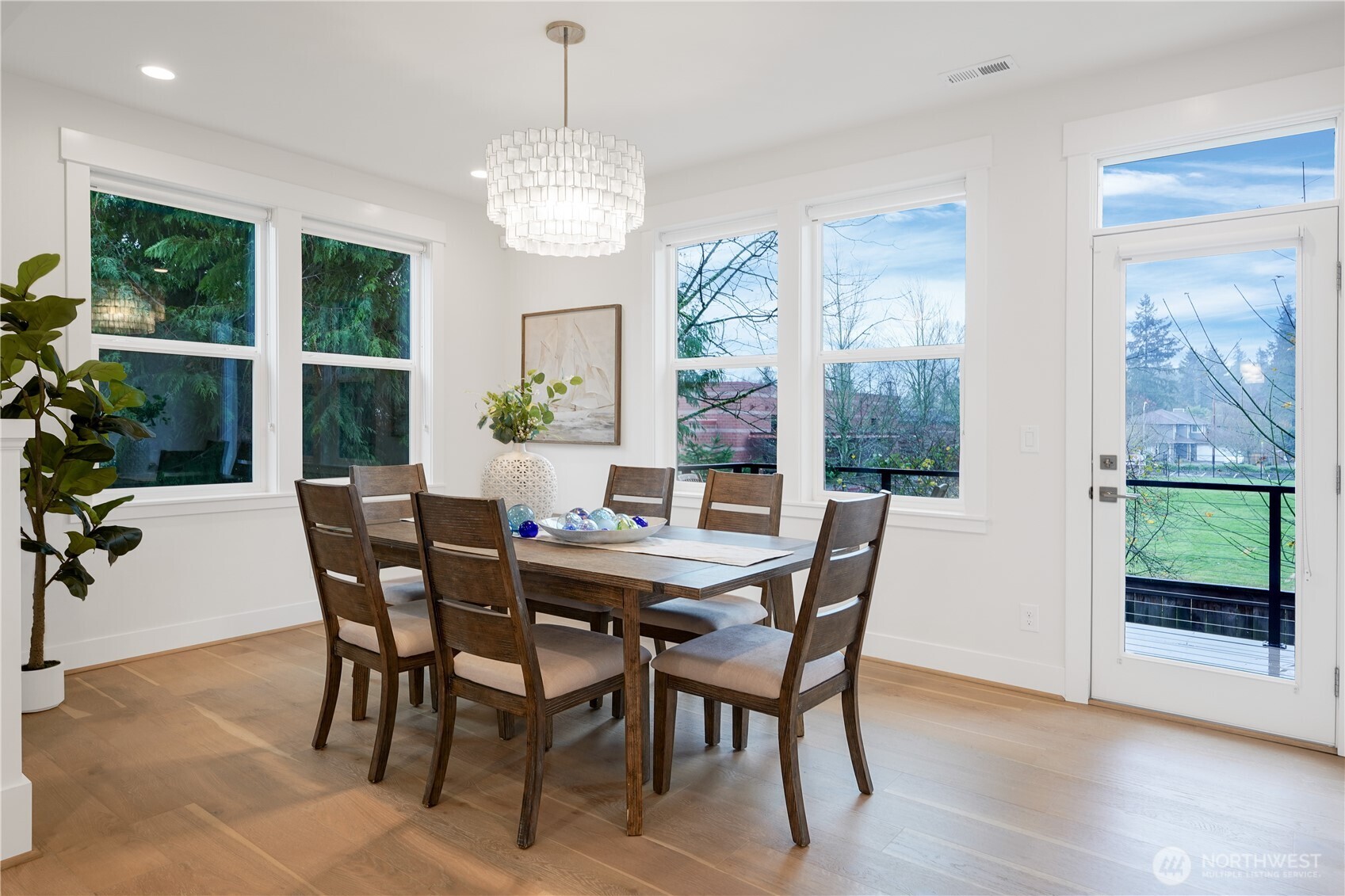 The dining area is bathed in natural light, with serene views over the deck and green field beyond.  A nearby door opens directly to the deck, seamlessly extending your living space and offering the opportunity to enjoy the outdoors.