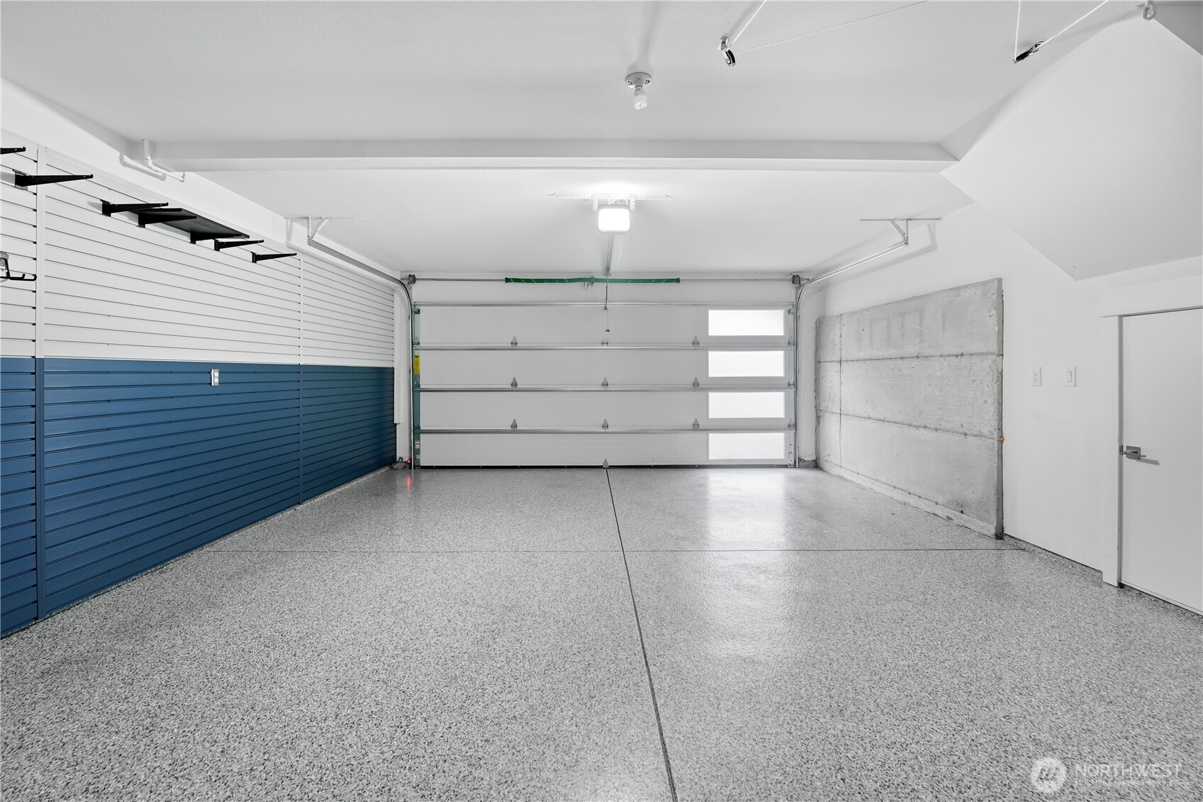 The garage is finished with durable epoxy flooring, offering both style and easy maintenance.  Walls are outfitted top-to-bottom with Slatwall customizable organizers, providing flexible storage solutions for every need.  Just beyond view, a built-in workbench with additional storage completes this highly functional space.