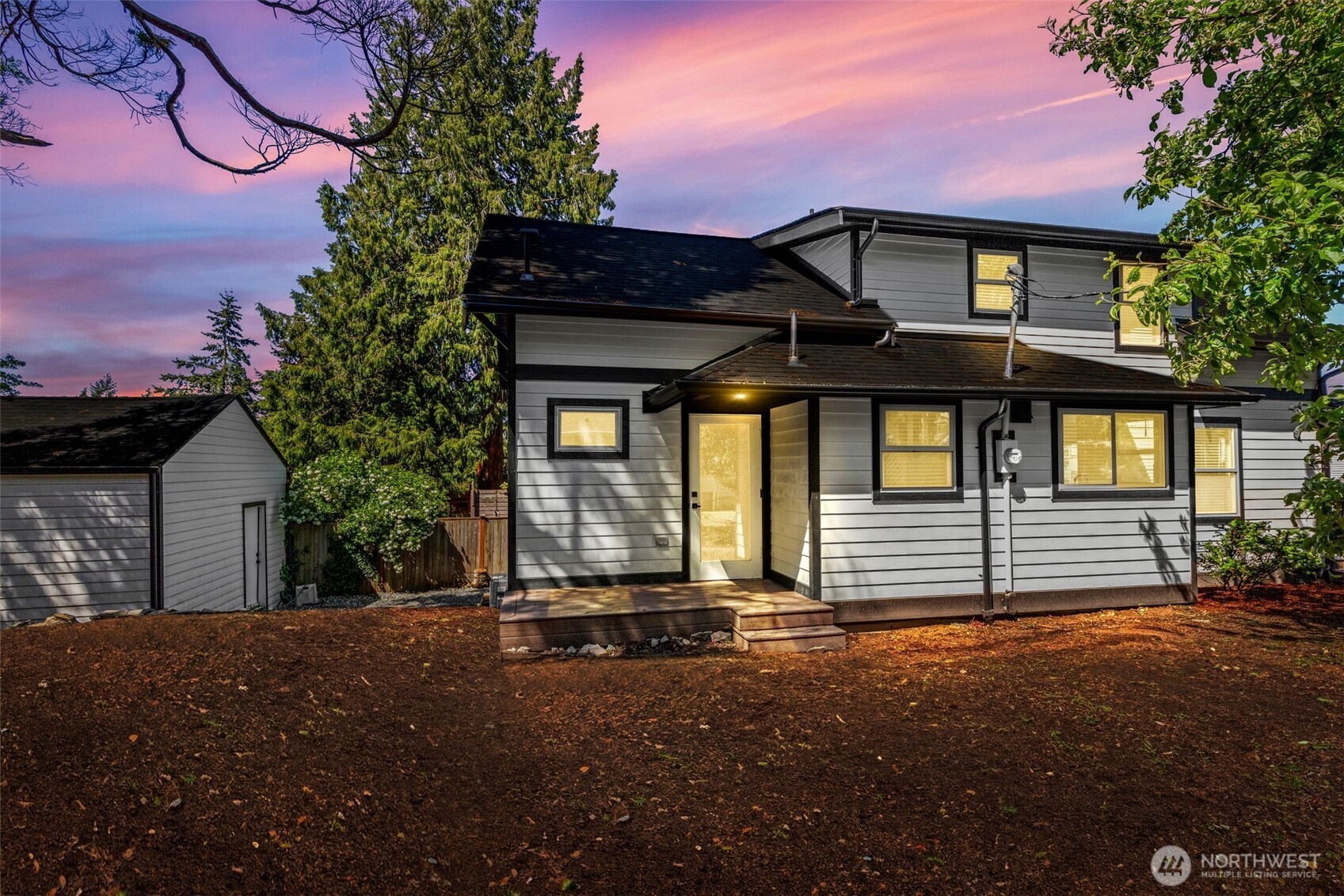 Twilight view of the back and side of the exterior, partially fenced.