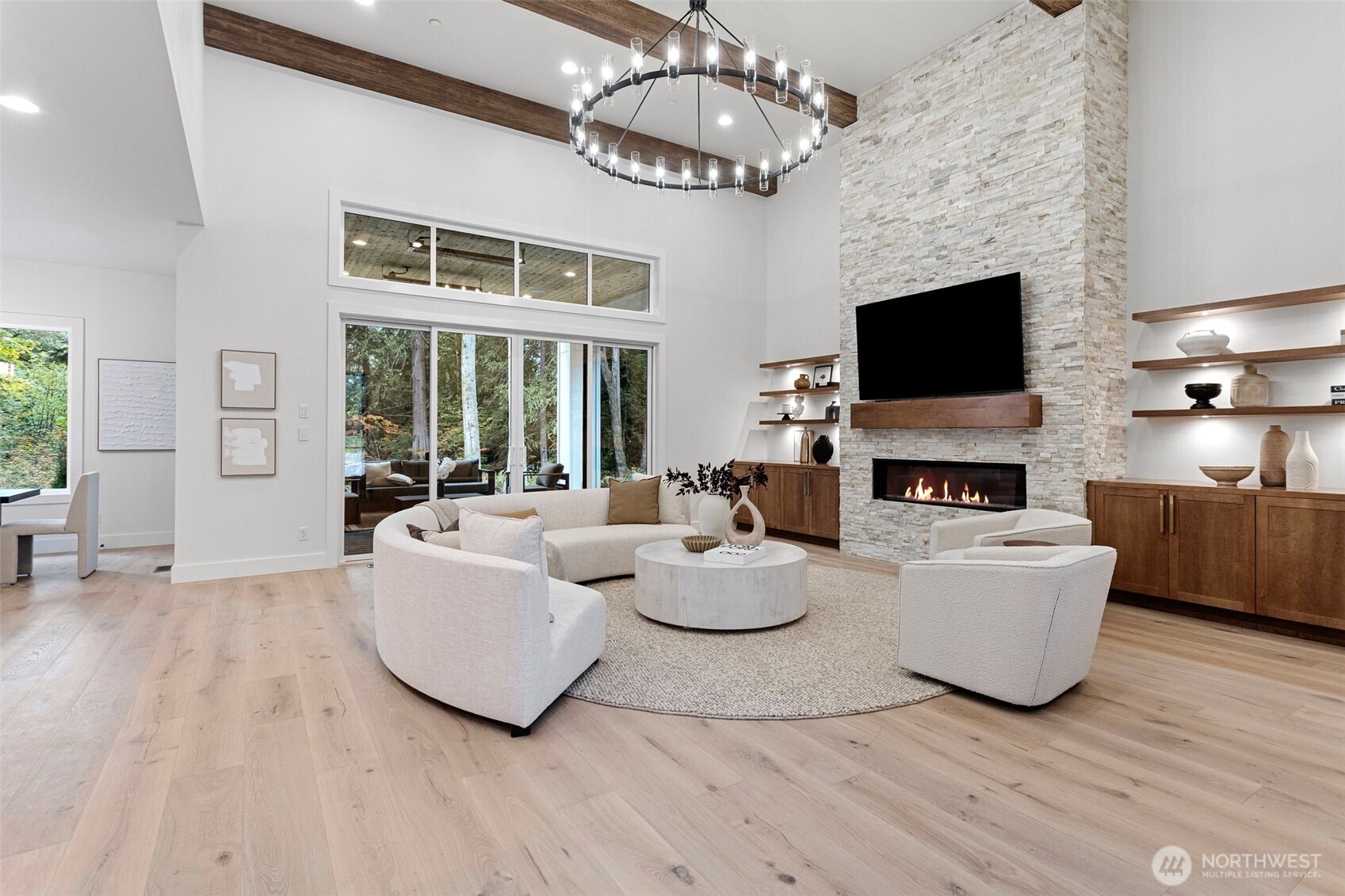Impressive great room with soaring 20’ ceilings and a grand sense of volume. A custom gas fireplace with a striking stone surround anchors the space, framed by bespoke cabinetry and illuminated shelving with integrated low-voltage lighting—creating warmth, sophistication, and style.