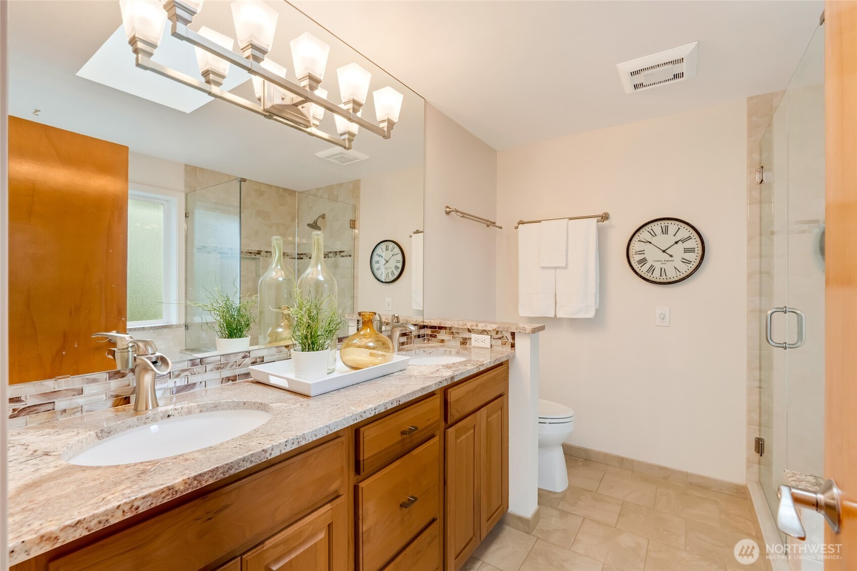 Beautifully remodeled ensuite bath featuring a dual-sink vanity with granite counters, modern lighting, and a walk-in shower with tile surround and glass enclosure.
