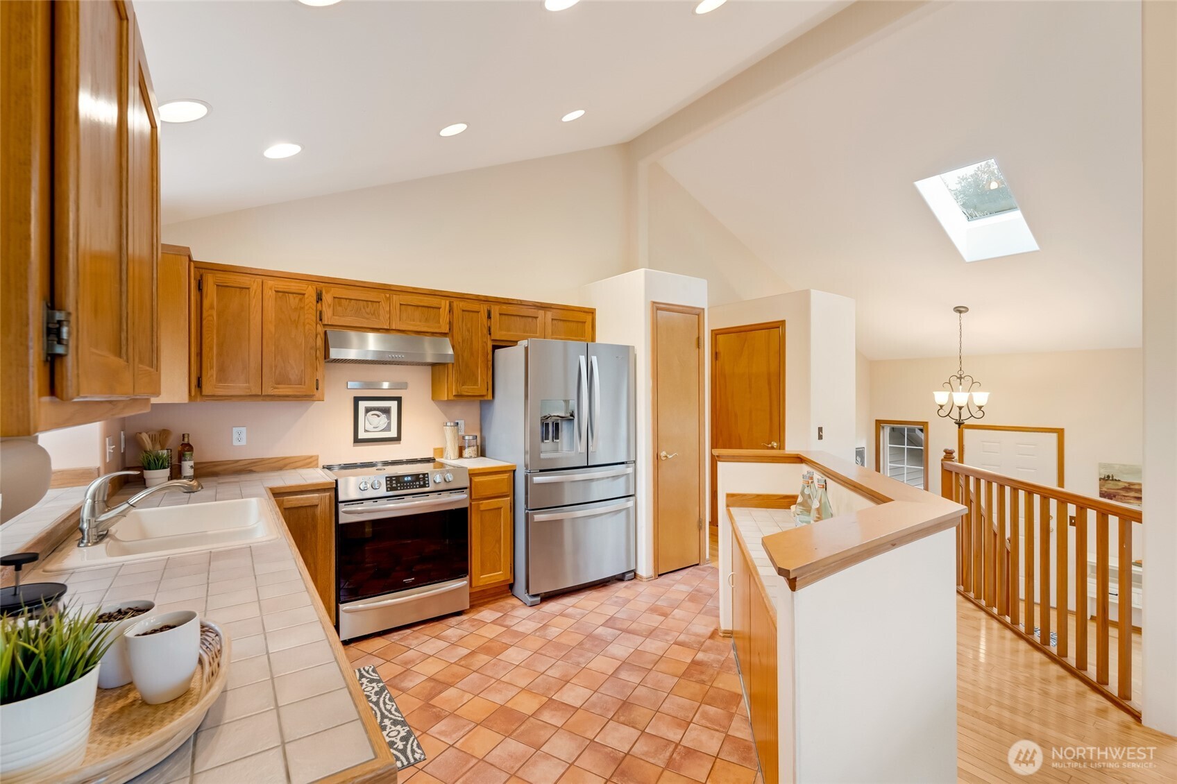 Spacious kitchen with vaulted ceilings, tile counters, and warm wood cabinetry. Modern stainless steel appliances and recessed lighting make this space both functional and inviting.