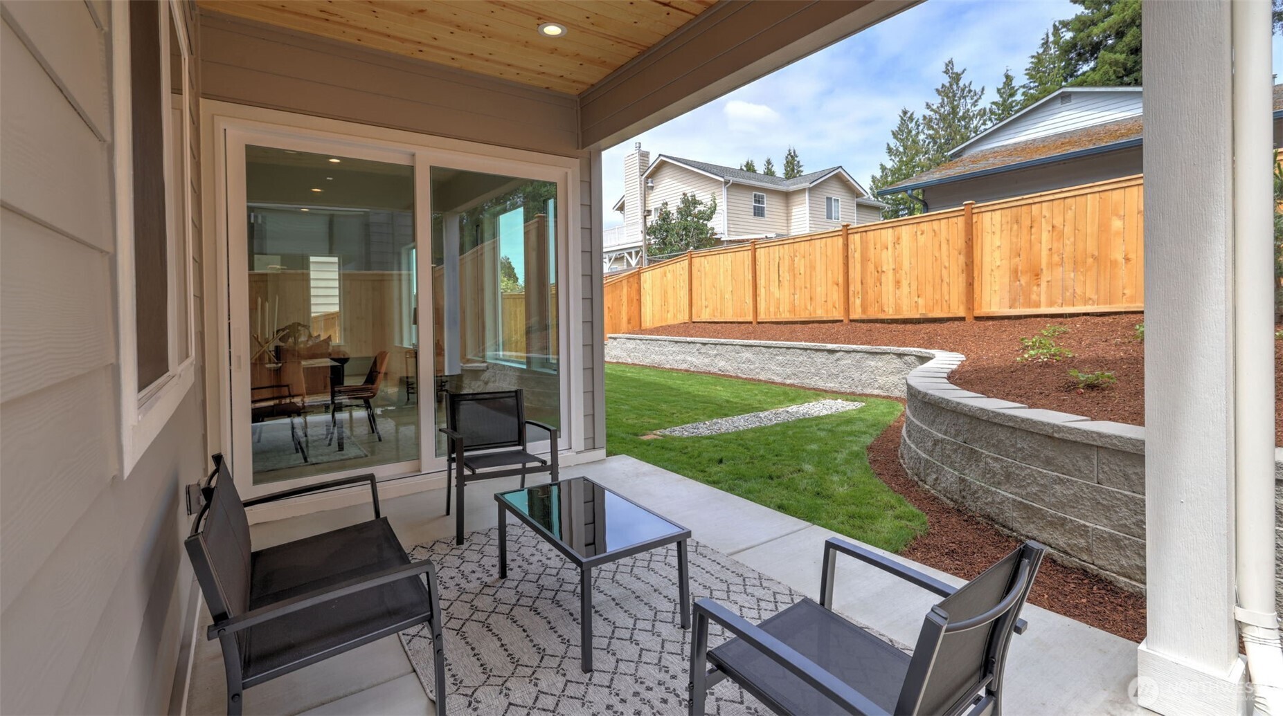 Expansive sliding doors open to a covered patio that extends living space outdoors — perfect for morning coffee or evening gatherings. The landscaped, fully fenced backyard is defined by tiered stonework and clean architectural lines, offering both beauty and privacy. With a lush lawn, sprinkler system and covered seating area, it’s a natural extension of the home’s bright, welcoming interior.