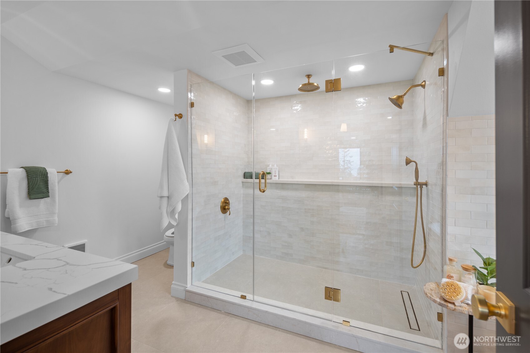 Another view of the Primary en suite bath - showing off the huge shower, gold fixtures, frameless glass enclosure and enviable full-length shelf!