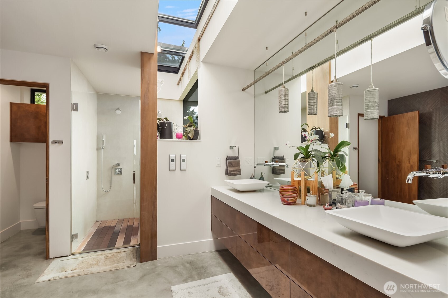 Luxurious primary bath features a floating vanity with vessel sinks and wall mount fixtures. Large, linear skylight illuminates the space with natural light. Dual shower with multiple heads and programmable temperature controls.