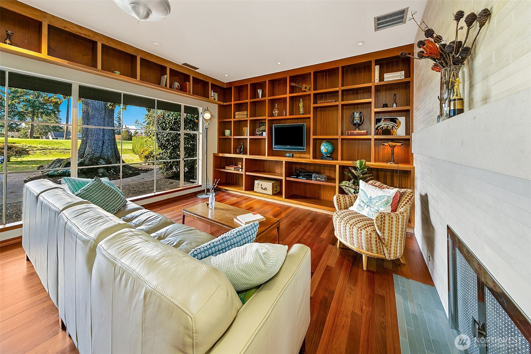 Custom mahogany casework defines the Great Room, wrapping the space in warm craftsmanship while the full-length steel window wall opens it to the Lanai and heritage oak. The result is a light-filled room shaped for gathering, reading and quiet connection to the landscape.