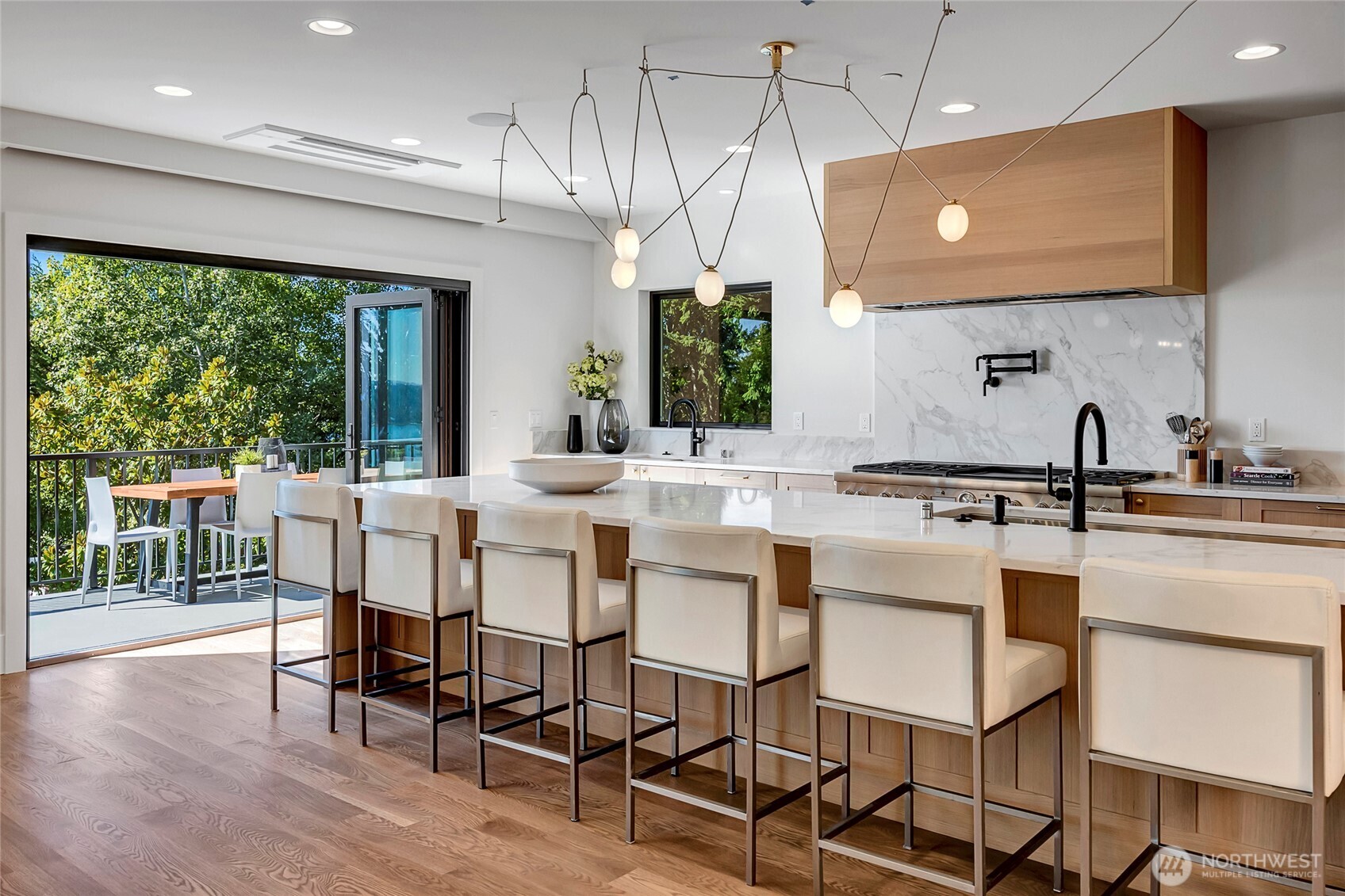 two large NanaWall doors that fold open to create a seamless indoor-outdoor flow. The huge quartz waterfall island, sleek cabinetry, and modern lighting make the space feel bright, open, and perfect for gathering.