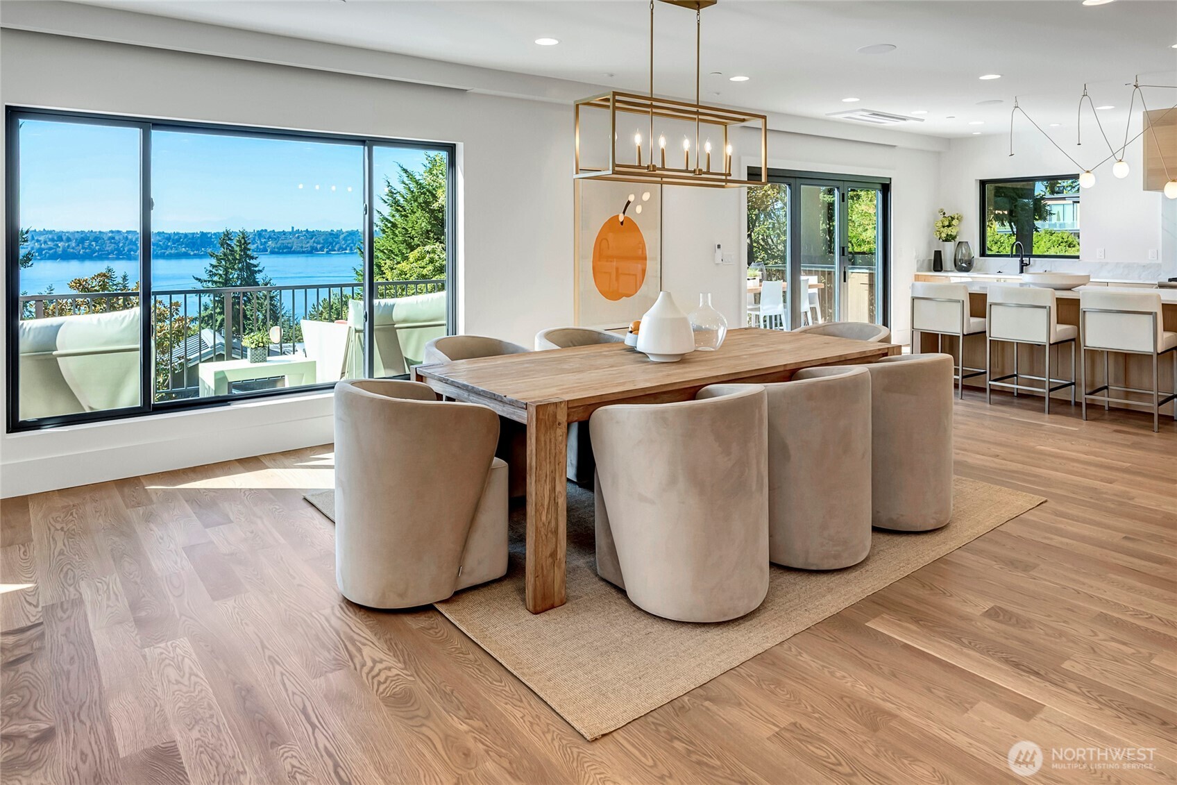The dining area sits seamlessly within the open great room, framed by sweeping western views of the lake, mountains and city. A custom modern light fixture anchors the space above the table, creating a warm centerpiece that complements the natural light pouring in through the expansive picture windows.