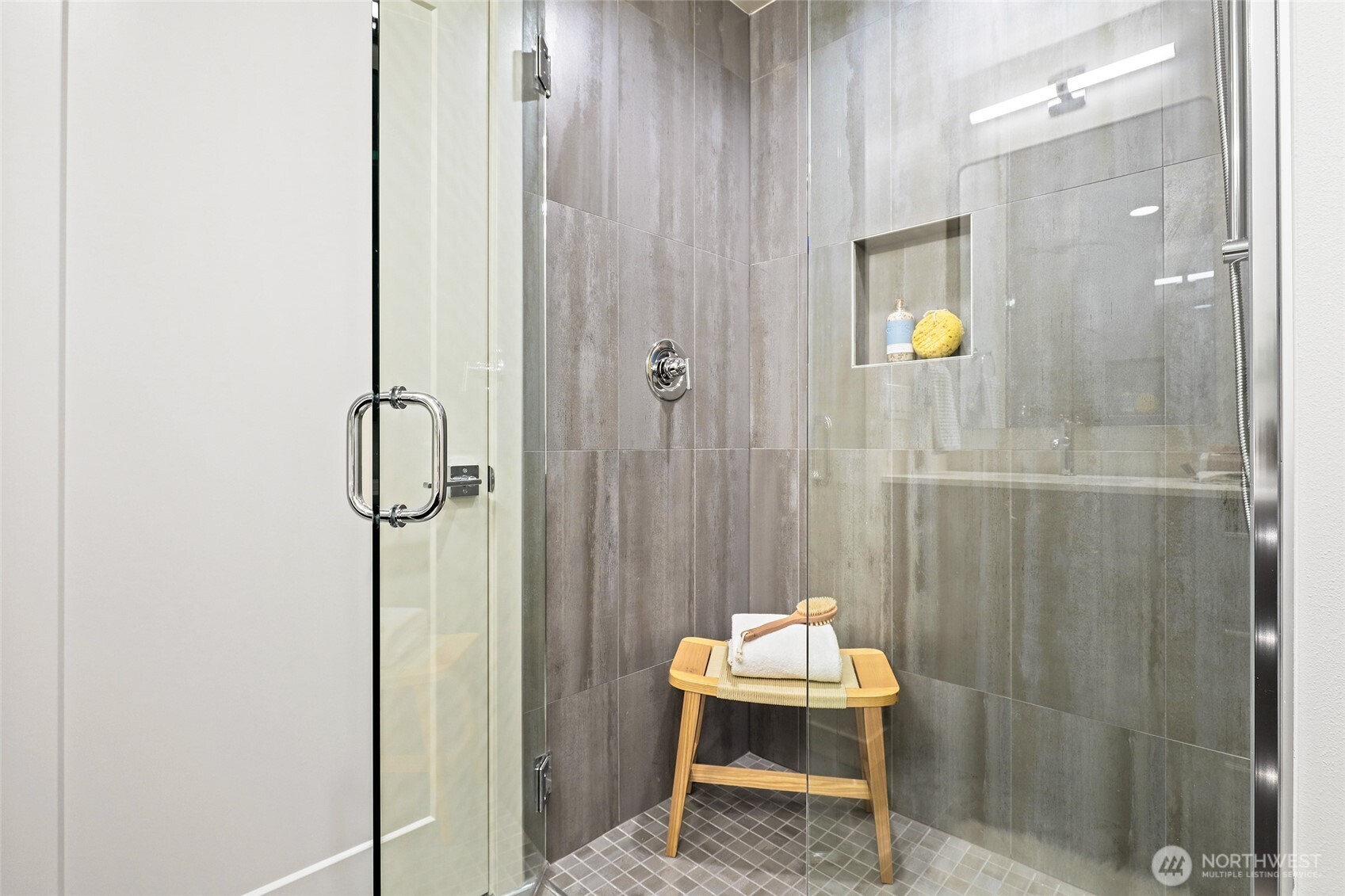This luxe walk-in shower features oversized tiles and glass doors, a built-in niche, and calming design touches.