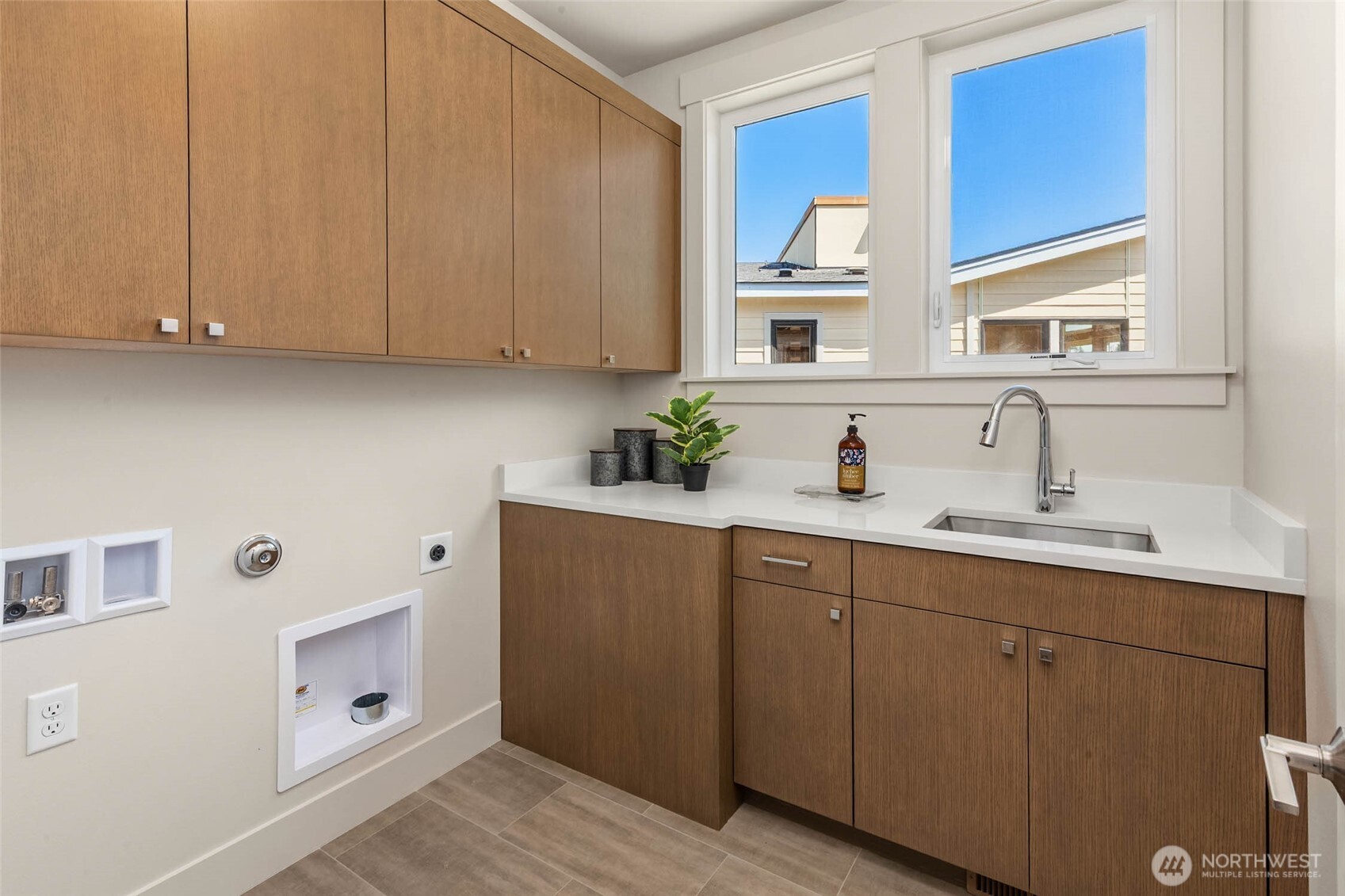 Well appointed laundry room with custom cabinets, slab counters, and under mounted steel sink
