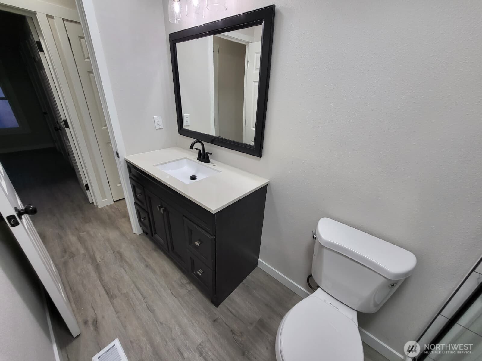 View of the vanity (and hallway) from the shower (dark room across is bedroom #2 we just saw). We are going to exit the bathroom and take a left, and immediately on our left will be bedroom #3.