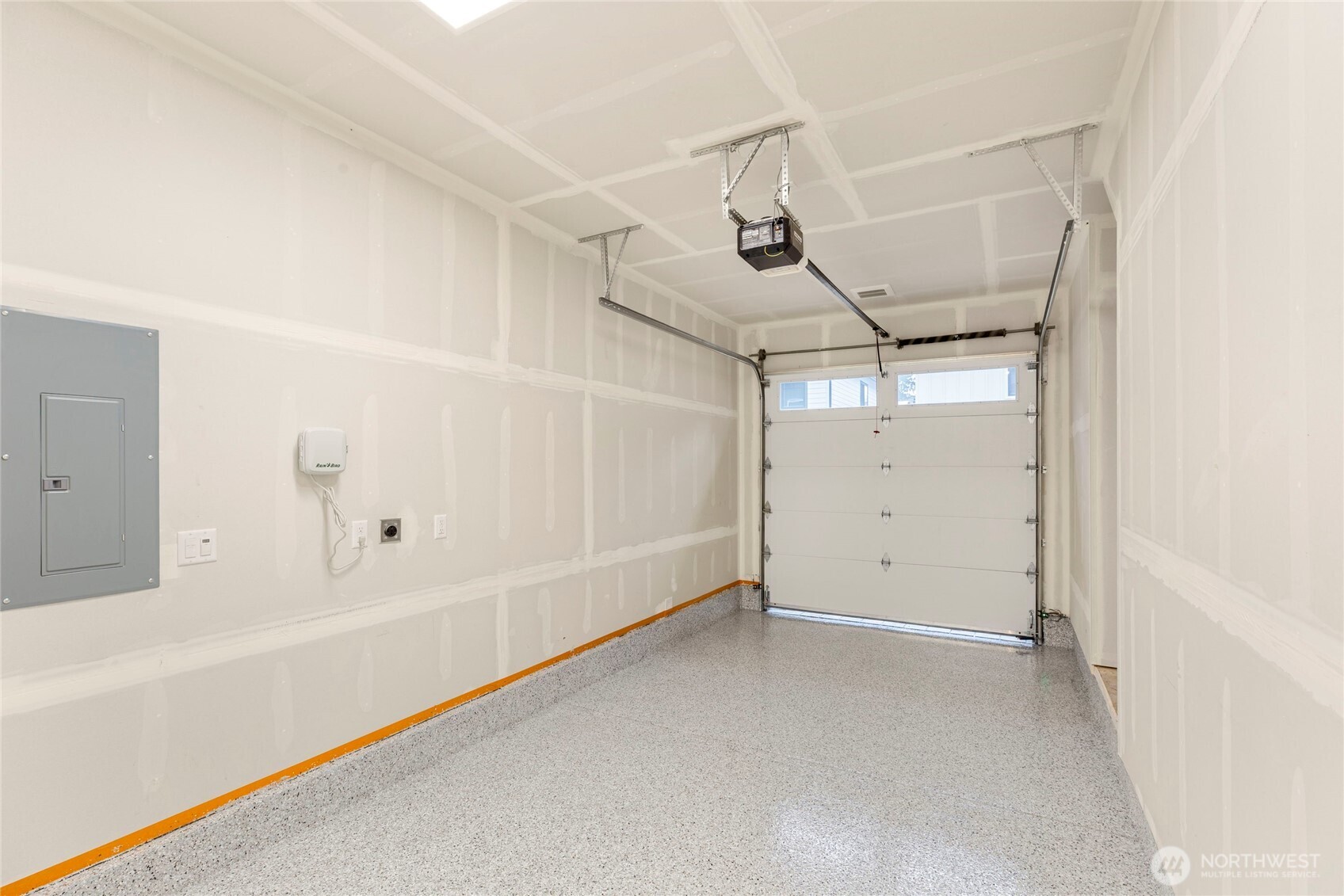 Garage with drywall finish, speckled epoxy flooring, ceiling-mounted opener, and sectional door with windows.