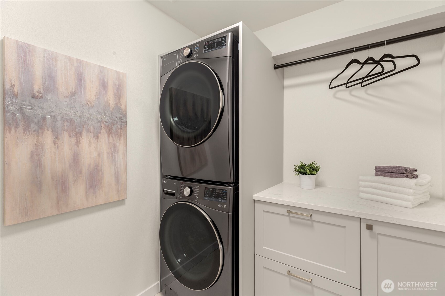 Laundry room with stacked washer and dryer, built-in cabinetry, countertop, and hanging rod.