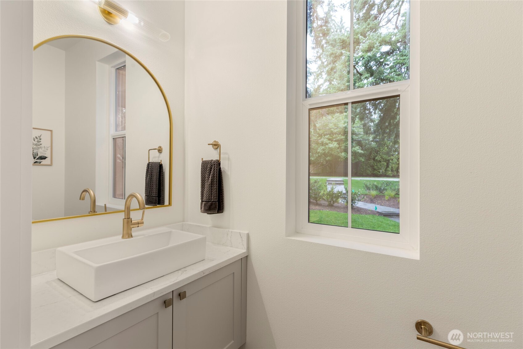 Elegant bathroom with marble countertop, gold accents, and arched mirror.
