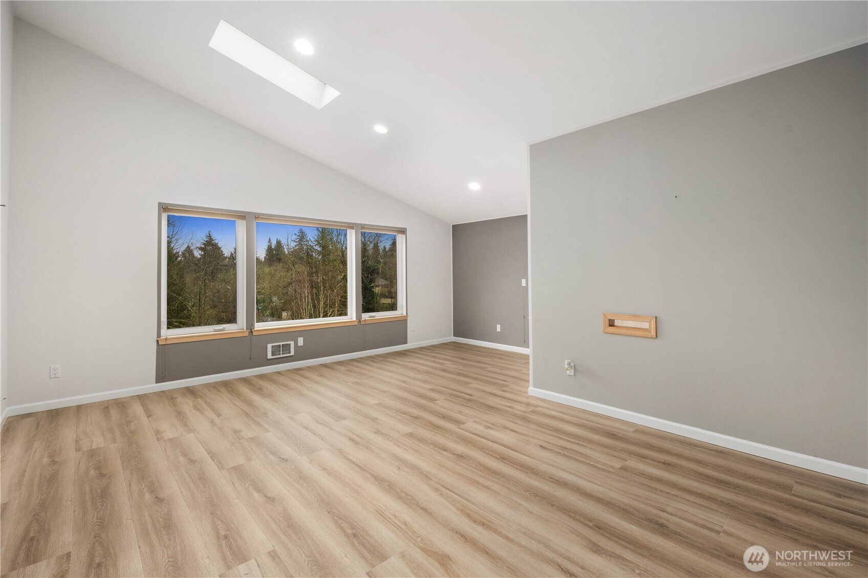 Bright bedroom featuring wide plank floors, large windows overlooking greenery, neutral tones, recessed lighting, and peaceful, airy atmosphere.