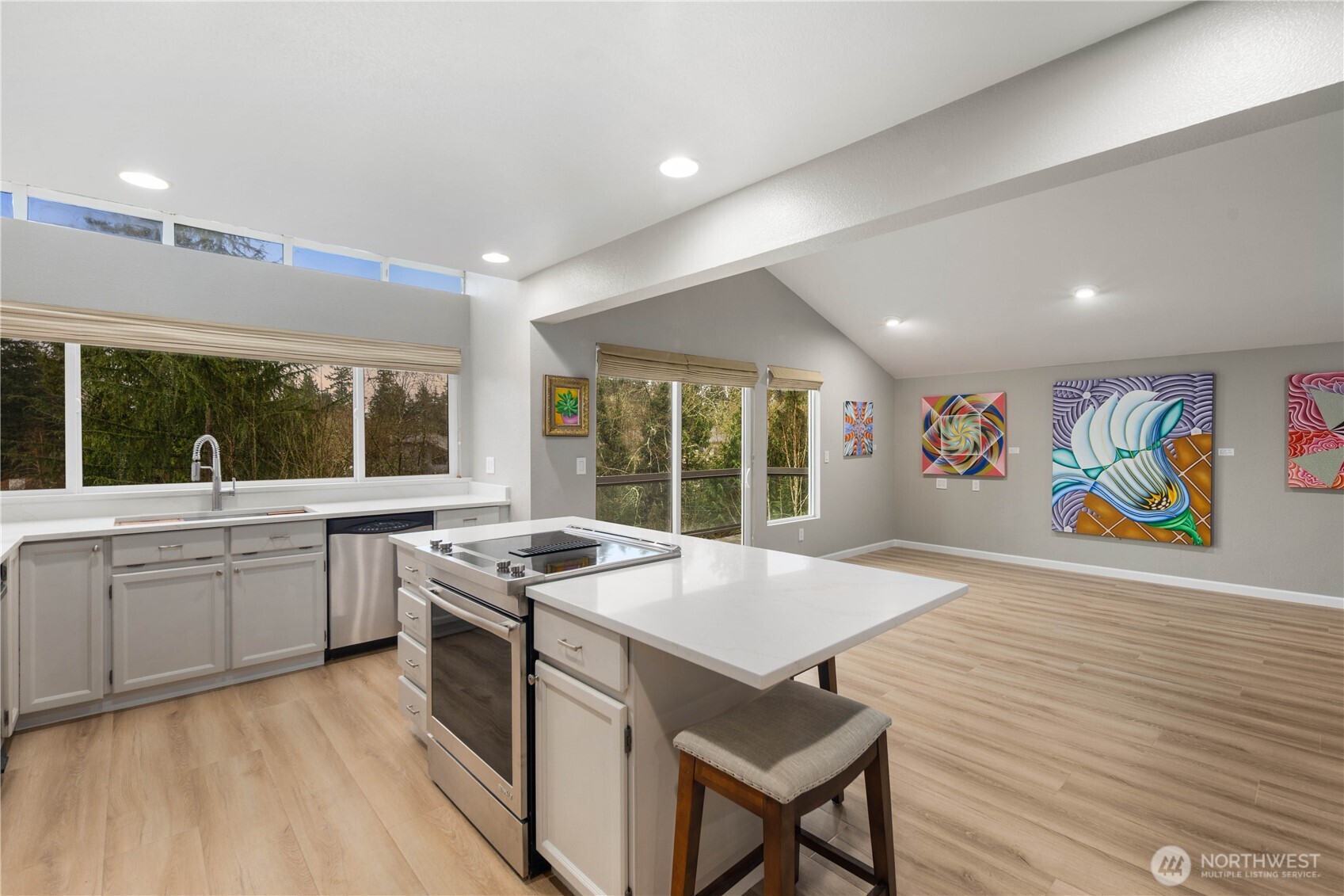 Spacious open living area with wide plank floors, vaulted ceilings, seamless kitchen flow, oversized windows, and inviting entertaining layout design.