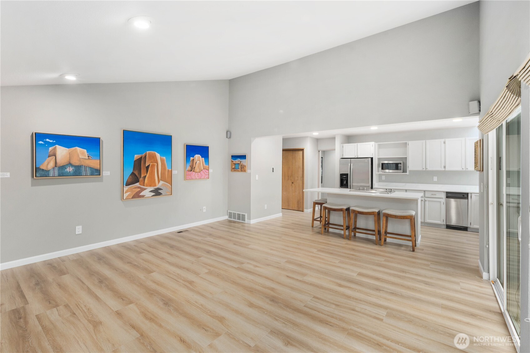 Bright open kitchen and living space with oversized island, seating, expansive windows, wide plank floors, and gallery-worthy wall art displays.