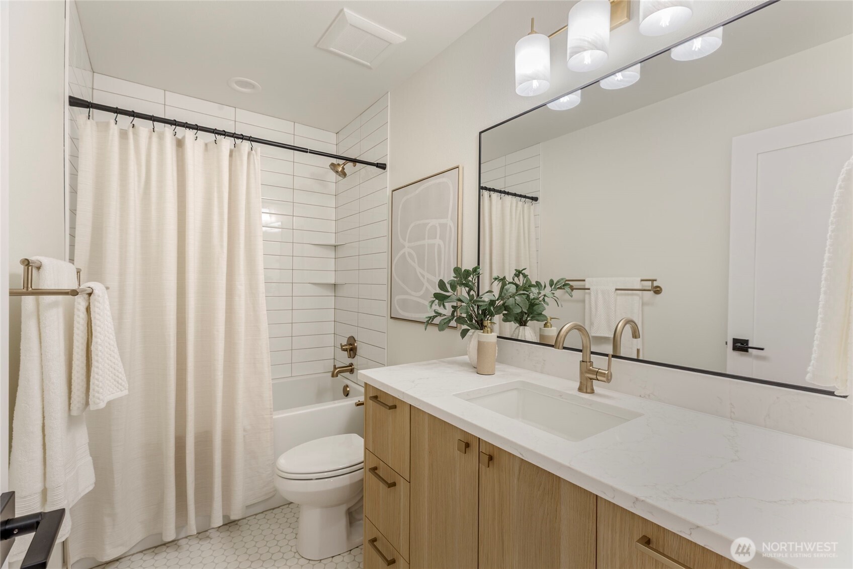 Bathroom with marble vanity, gold fixtures, subway tile shower, and hex tile flooring.