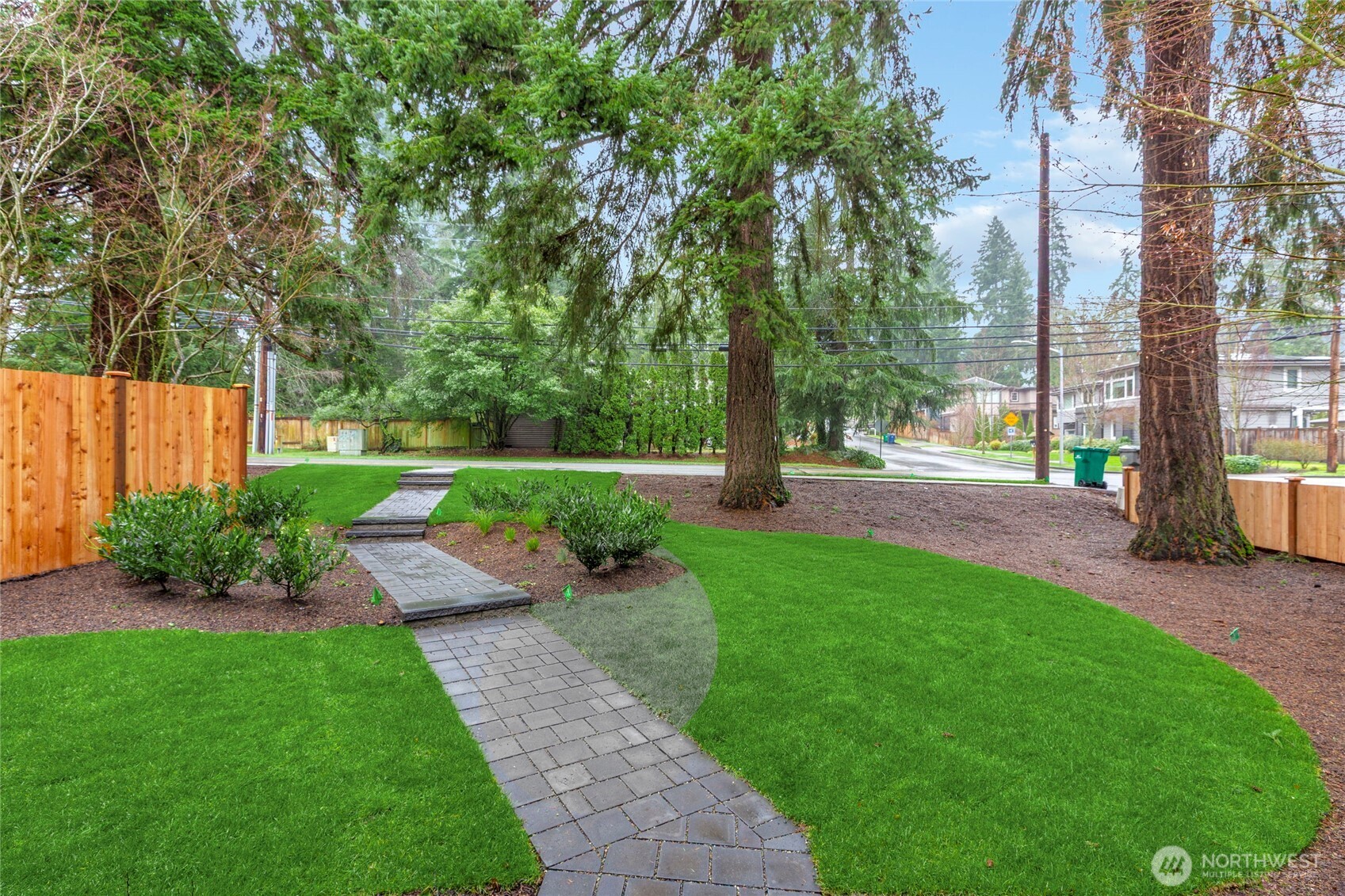 Neatly landscaped front yard with stone walkway, green lawn, and mature shade trees.
