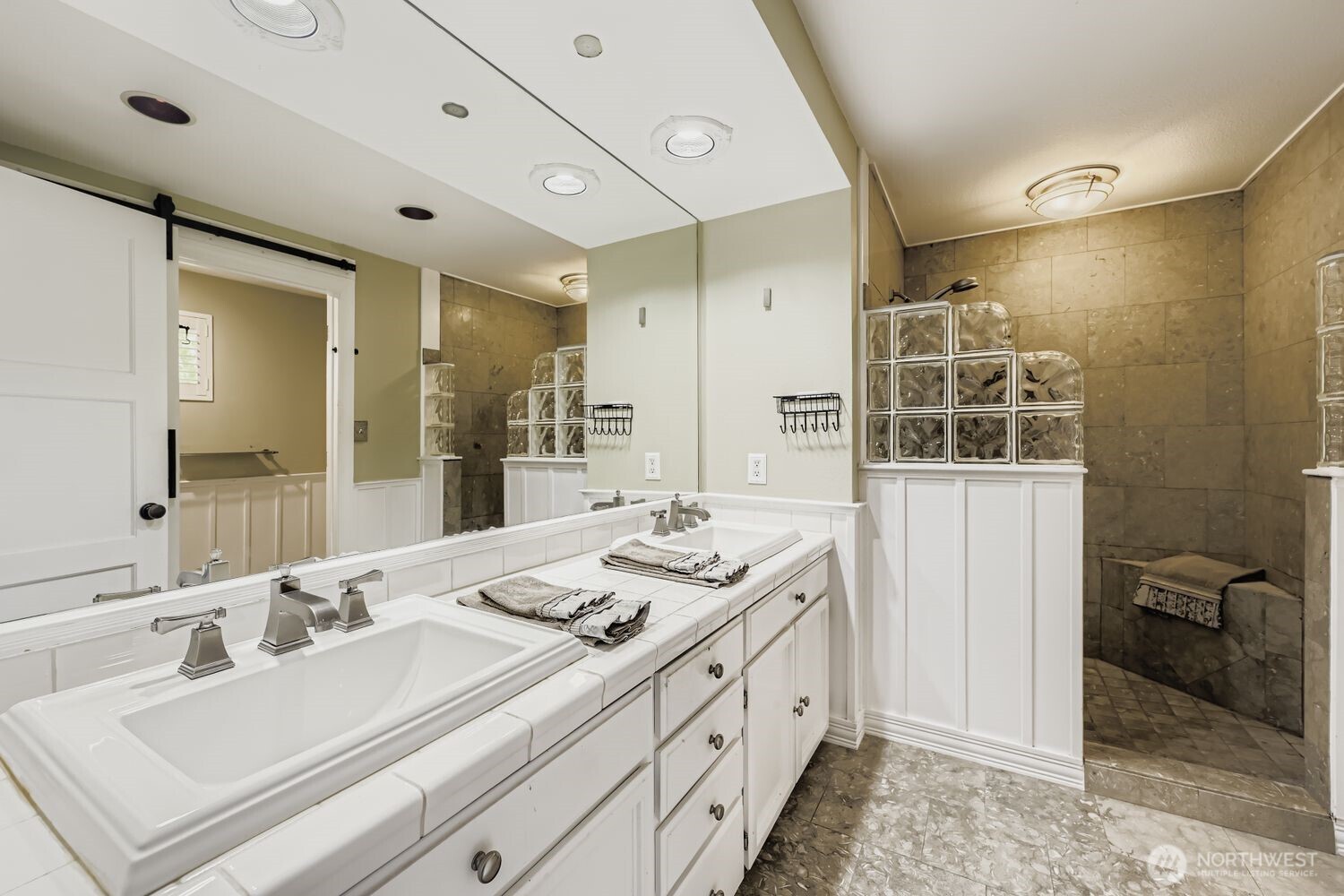 The well-designed Primary bath boasts a large walk-in tiled shower with glass blocks, dual sinks, excellent lighting, abundant cabinetry, tile countertops and flooring plus a separate & private water closet.