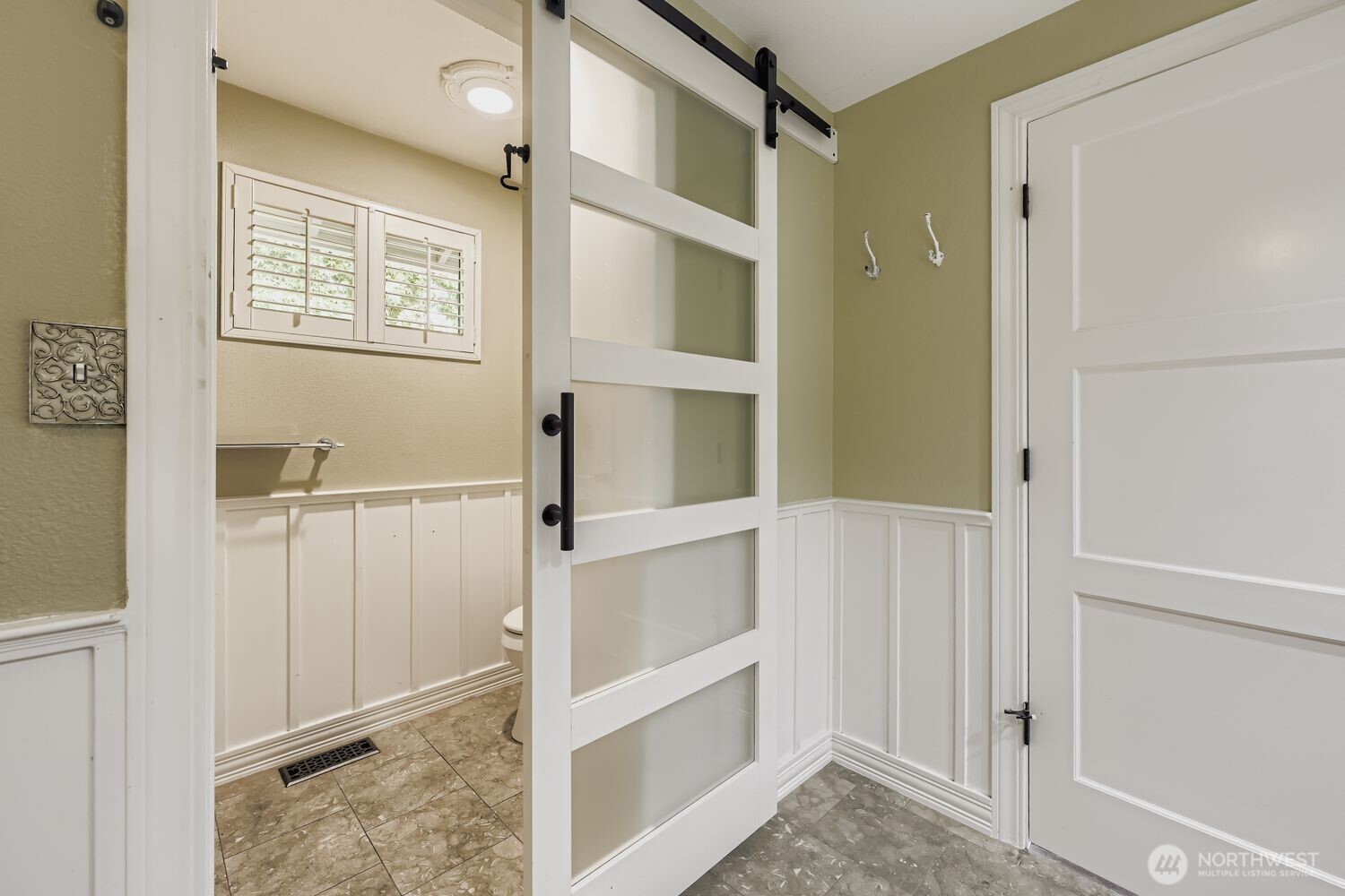 The WC is separated from the rest of the bathroom with an attractive barn door.  Wainscotting adds to the pleasing decor.